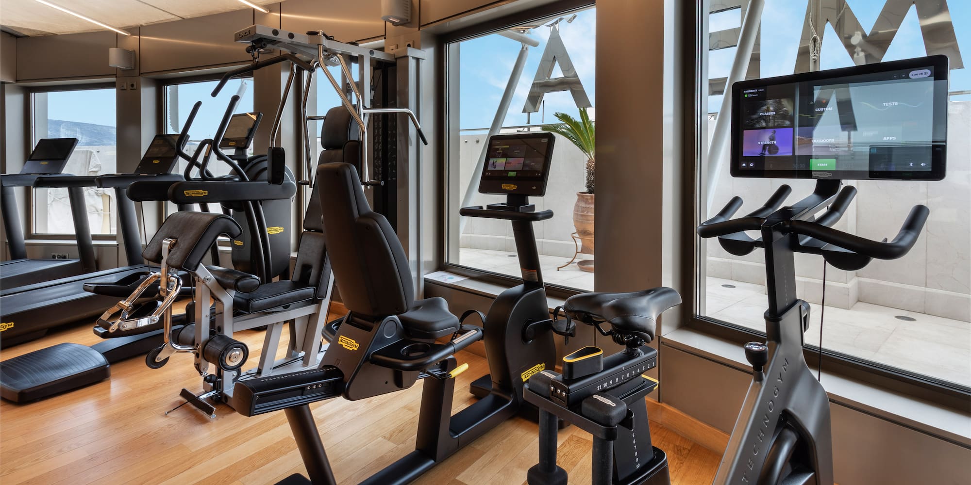 Modern fitness center with Technogym equipment and panoramic outdoor view.