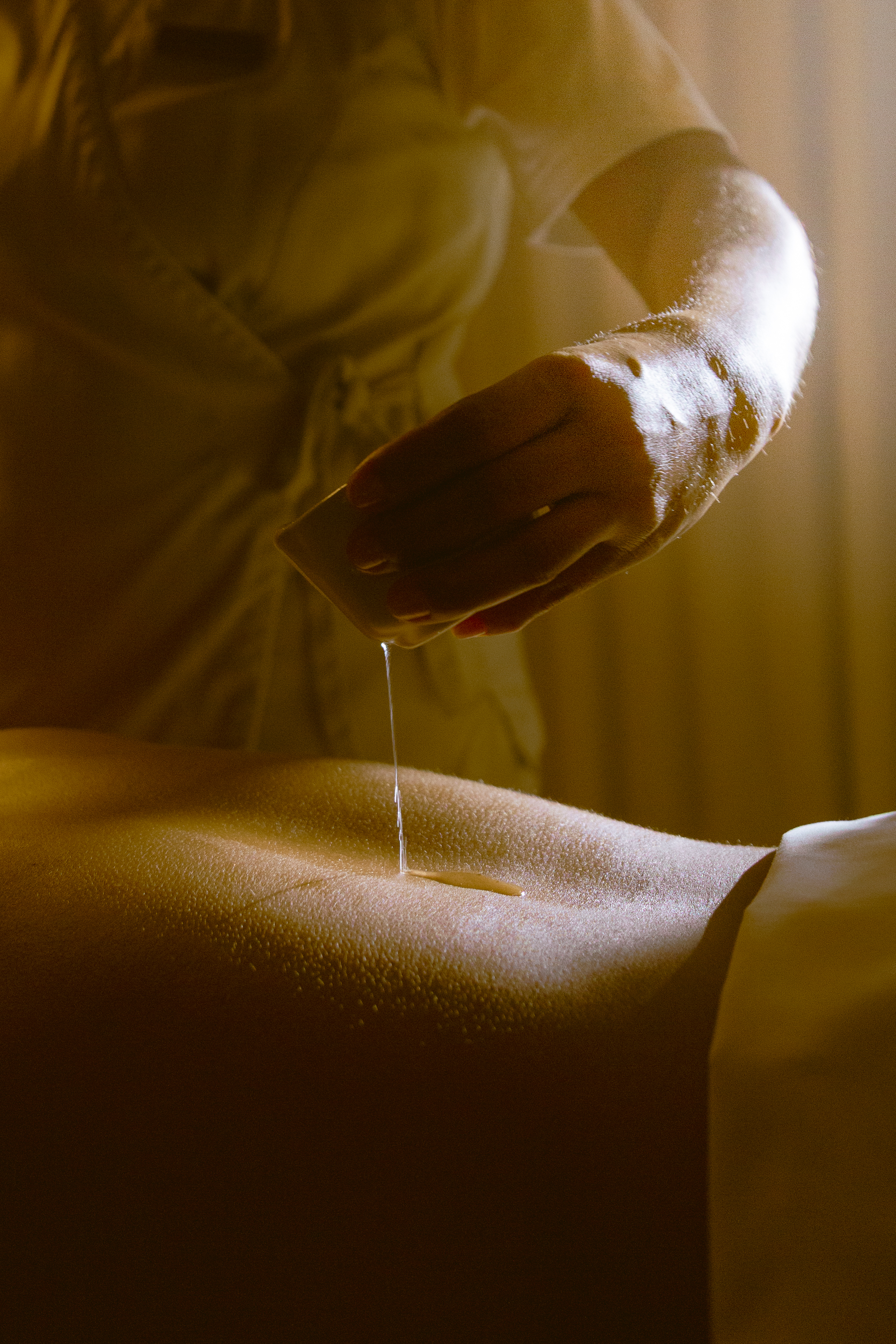 Spa therapist pouring massage oil onto a client's back for relaxation treatment.