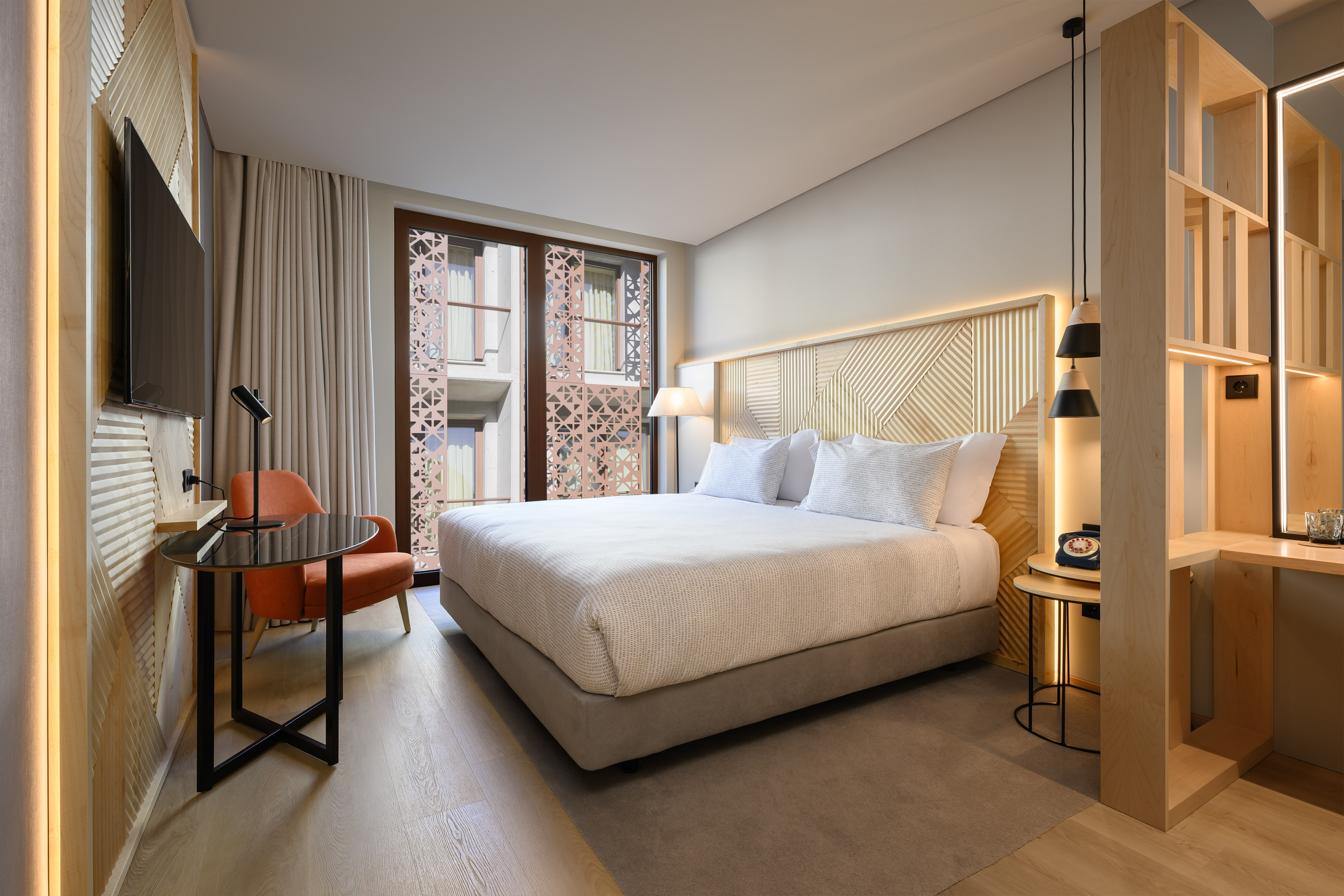 Contemporary hotel bedroom with patterned wood headboard, bed, and window.