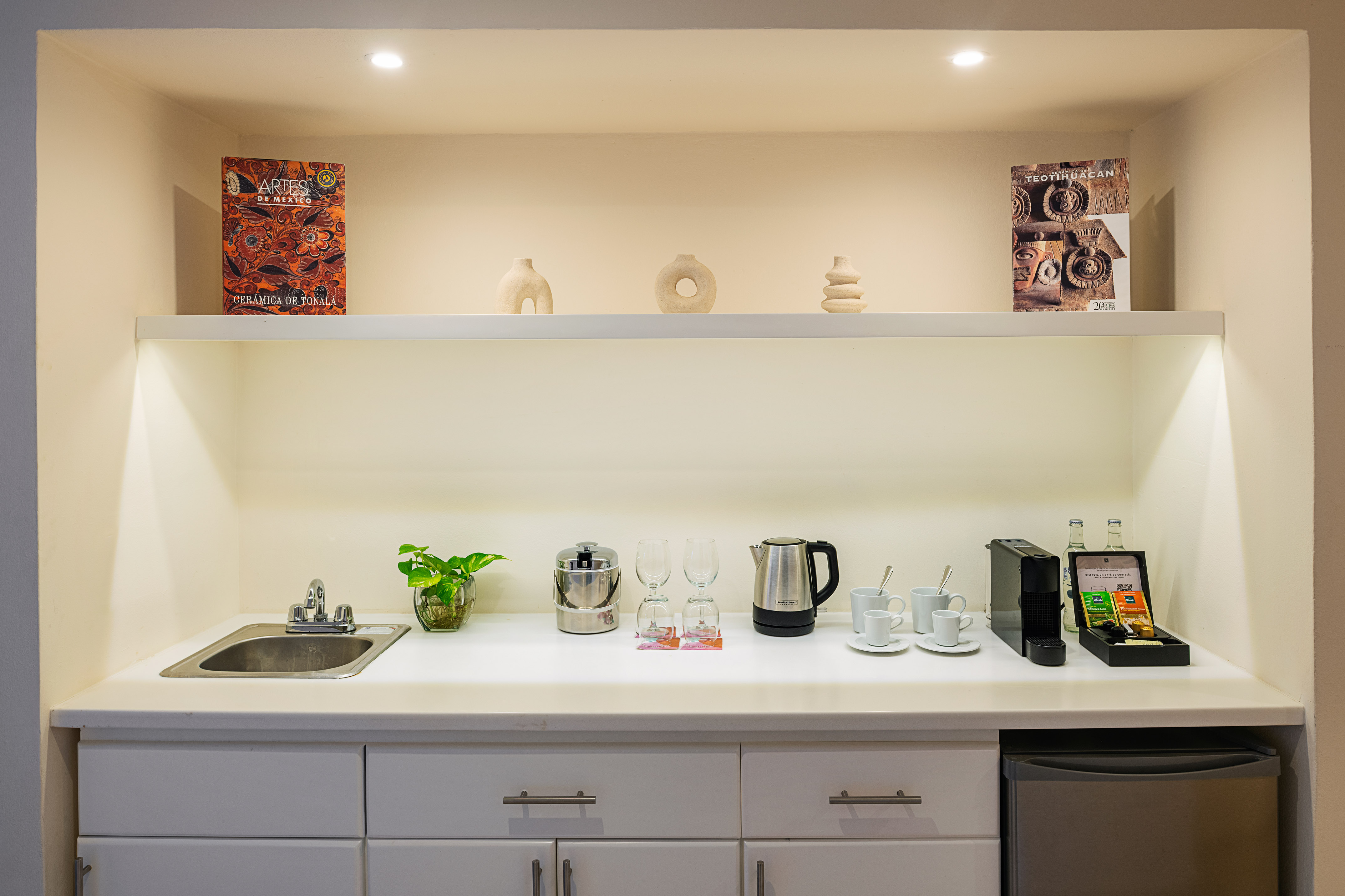 Compact hotel kitchenette with coffee maker, kettle, sink, and stylish decor.
