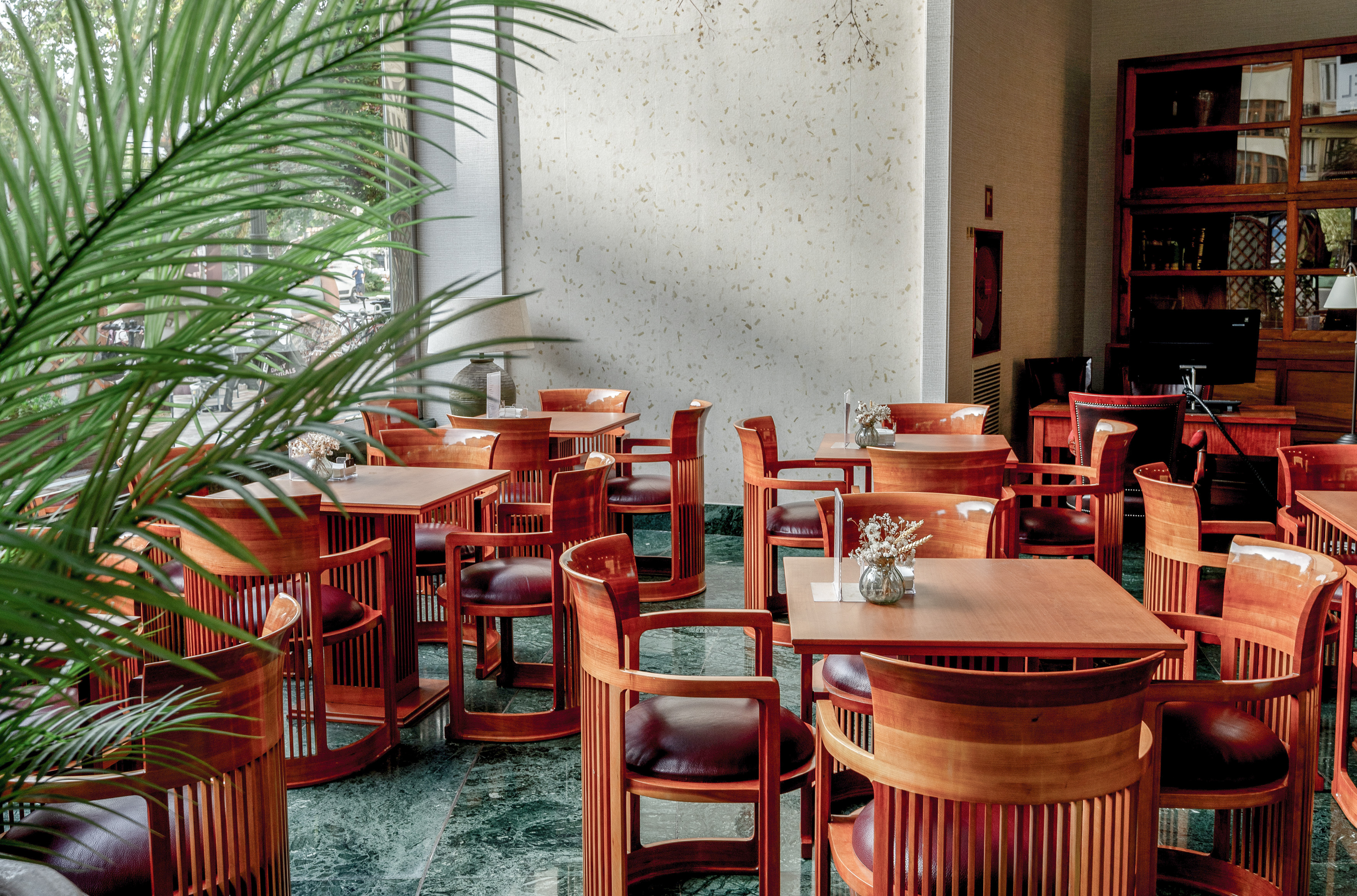 Hotel lounge, wooden tables, leather chairs, green marble floor, and palm.
