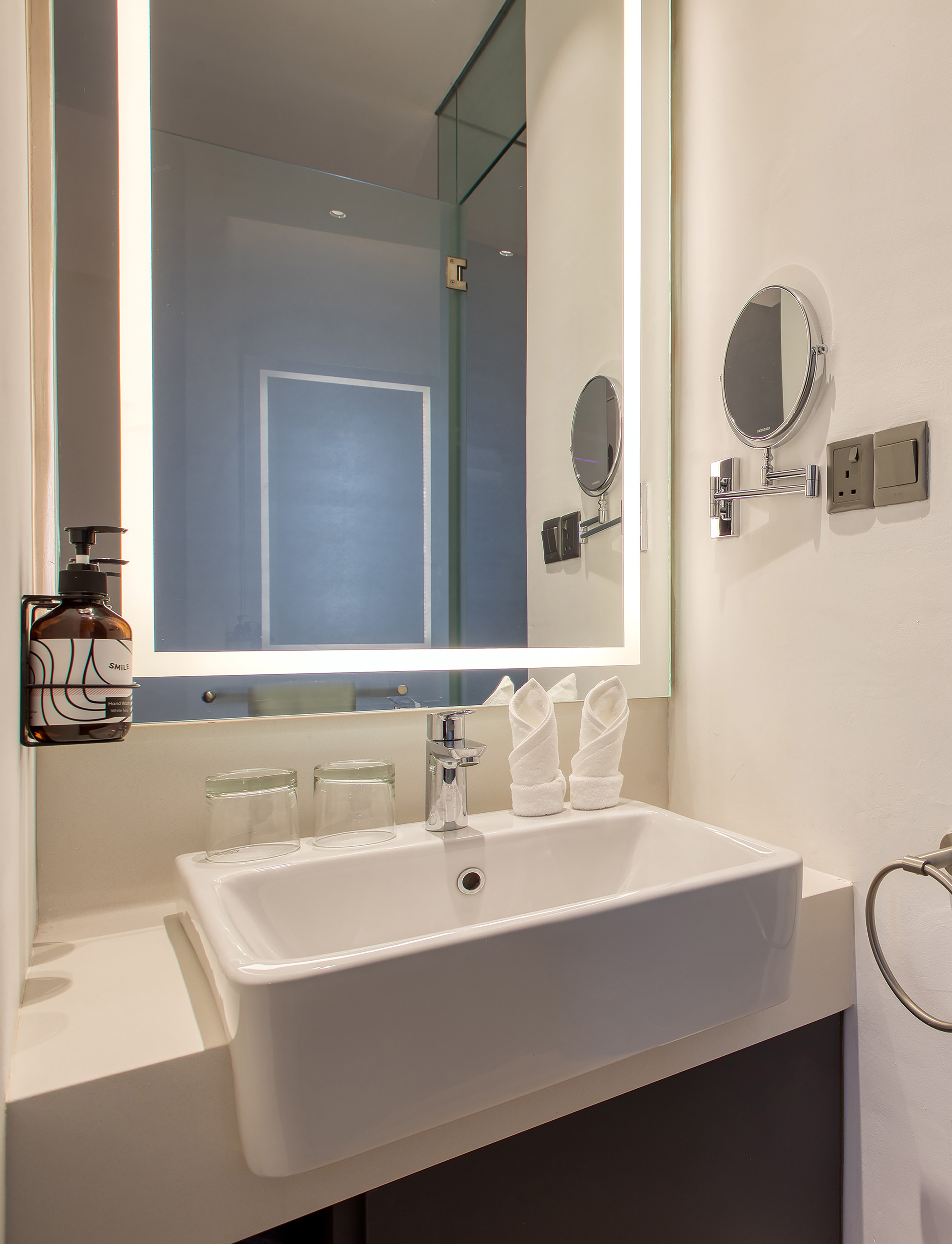Hotel bathroom vanity with white sink, backlit mirror, chrome faucet, towels.