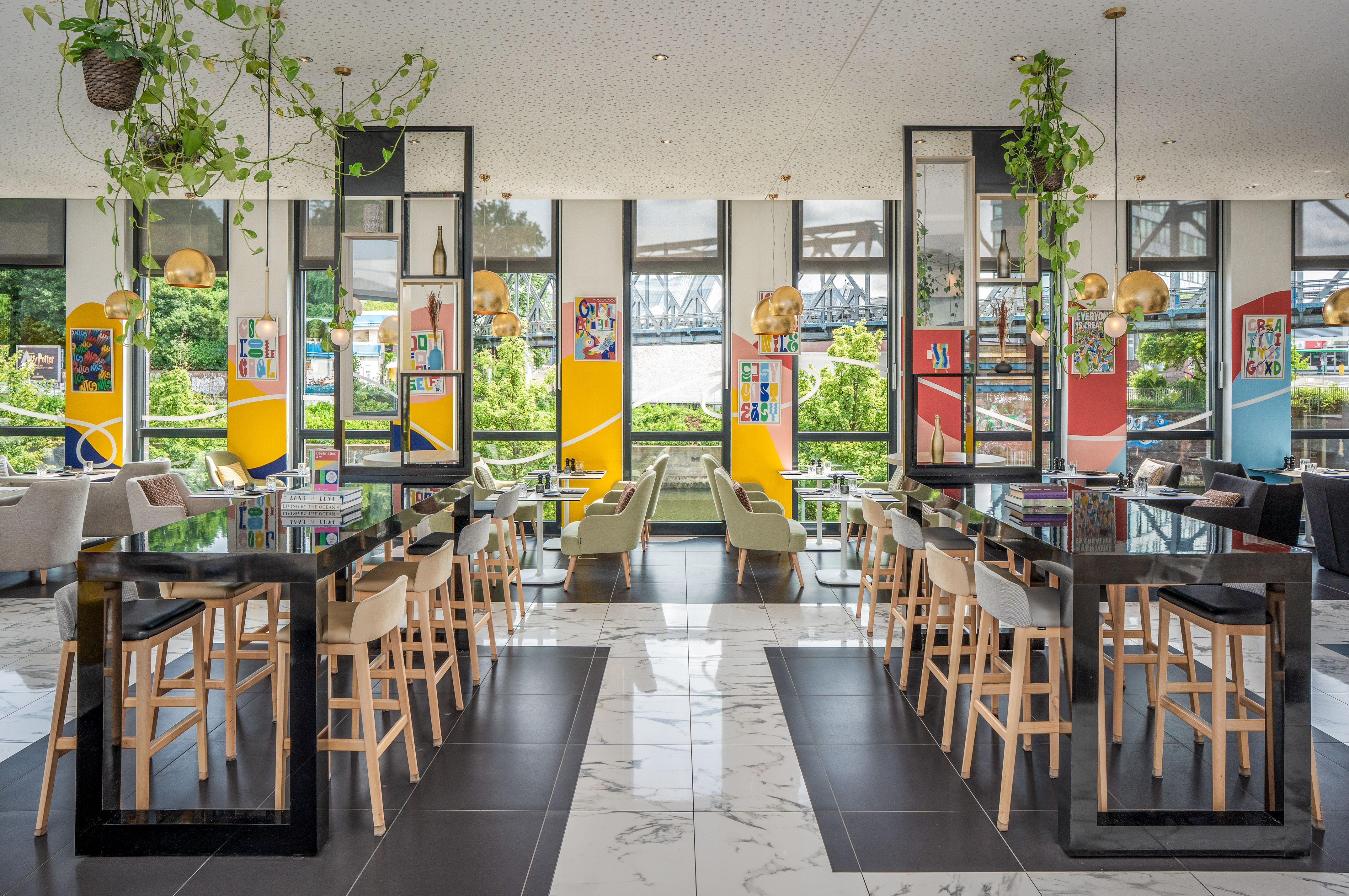 Modern restaurant with high tables, lounge seating, vibrant decor, and large windows.