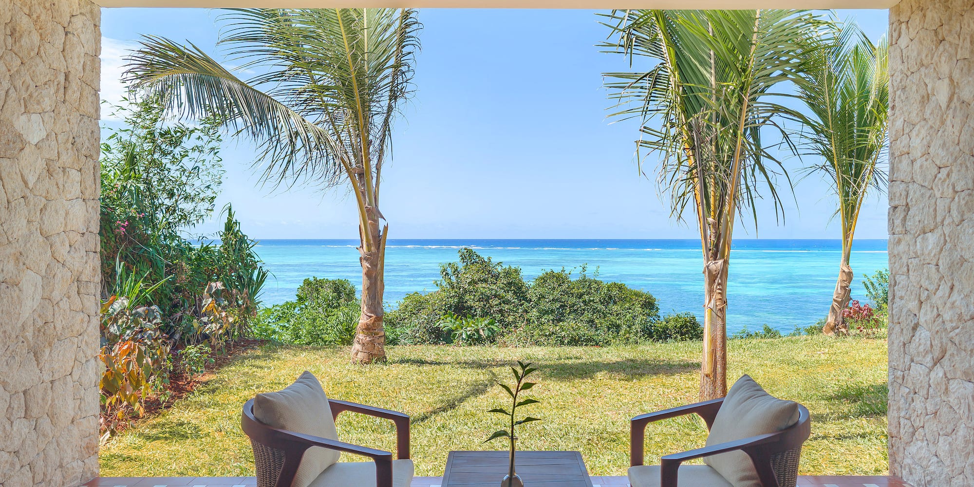 Tropical patio with ocean view, palm trees, and outdoor seating.