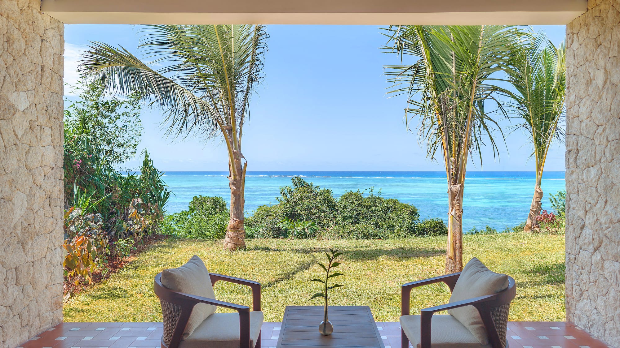 Tropical patio with ocean view, palm trees, and outdoor seating.