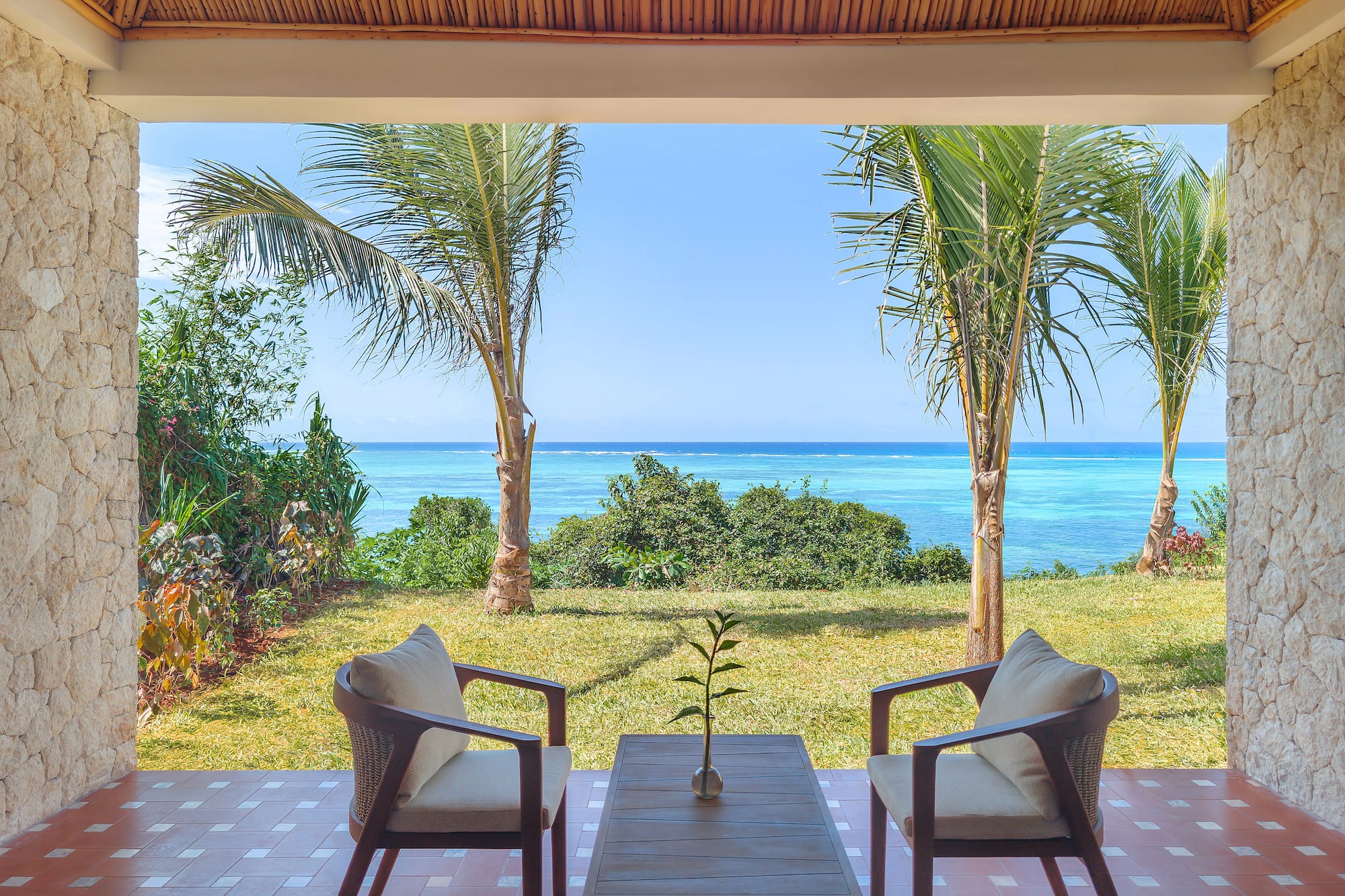 Tropical patio with ocean view, palm trees, and outdoor seating.