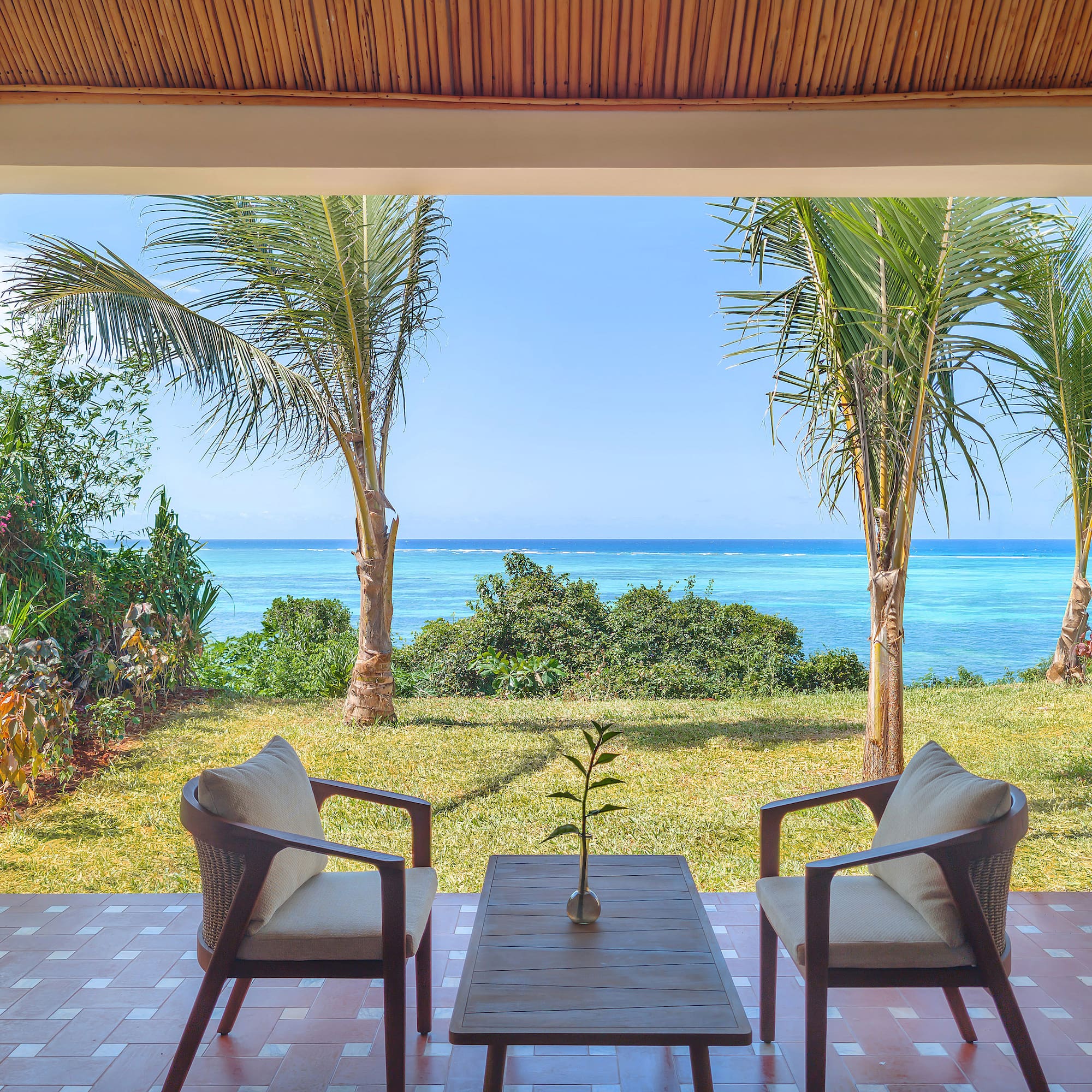 Tropical patio with ocean view, palm trees, and outdoor seating.
