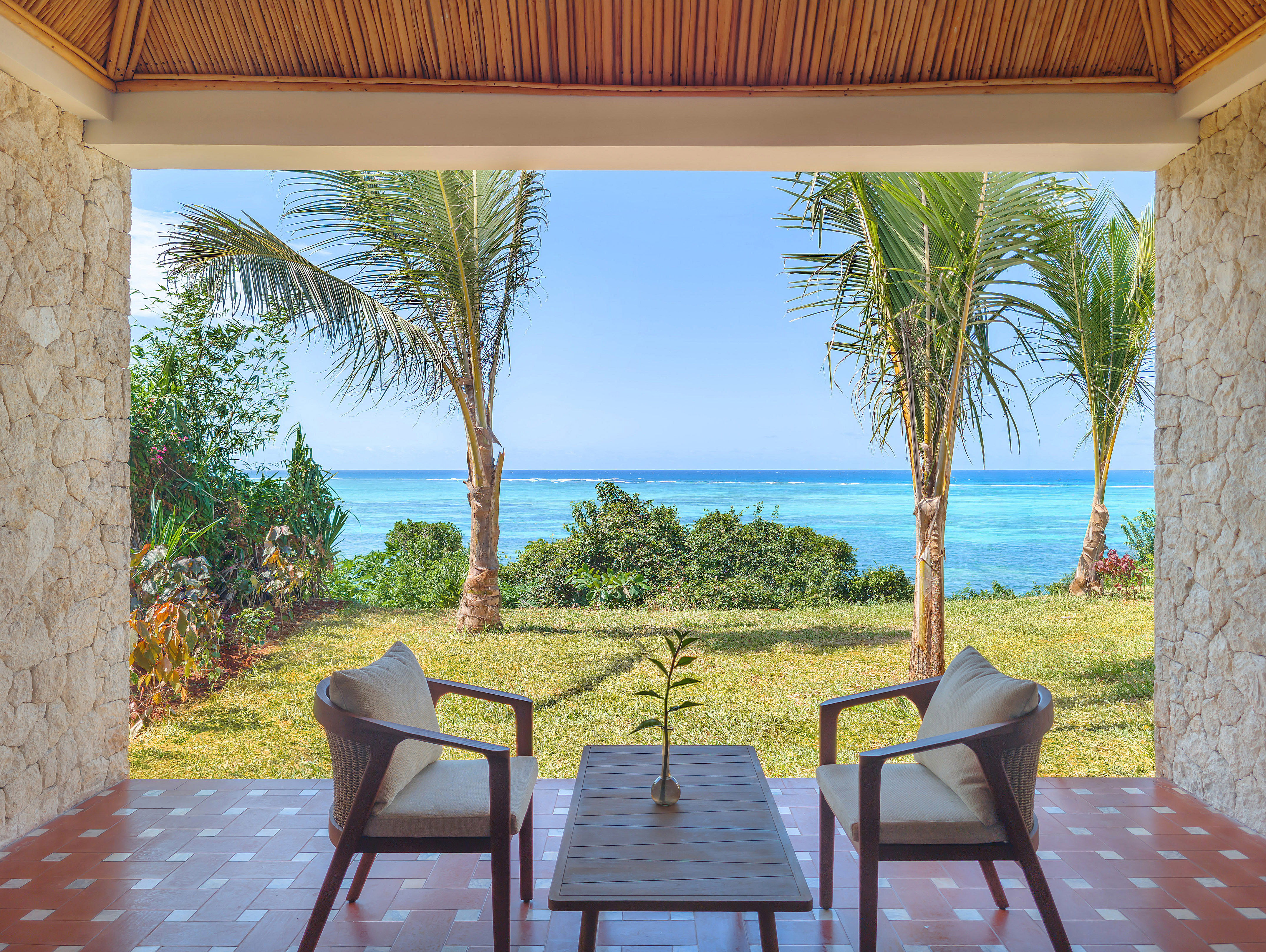 Tropical patio with ocean view, palm trees, and outdoor seating.