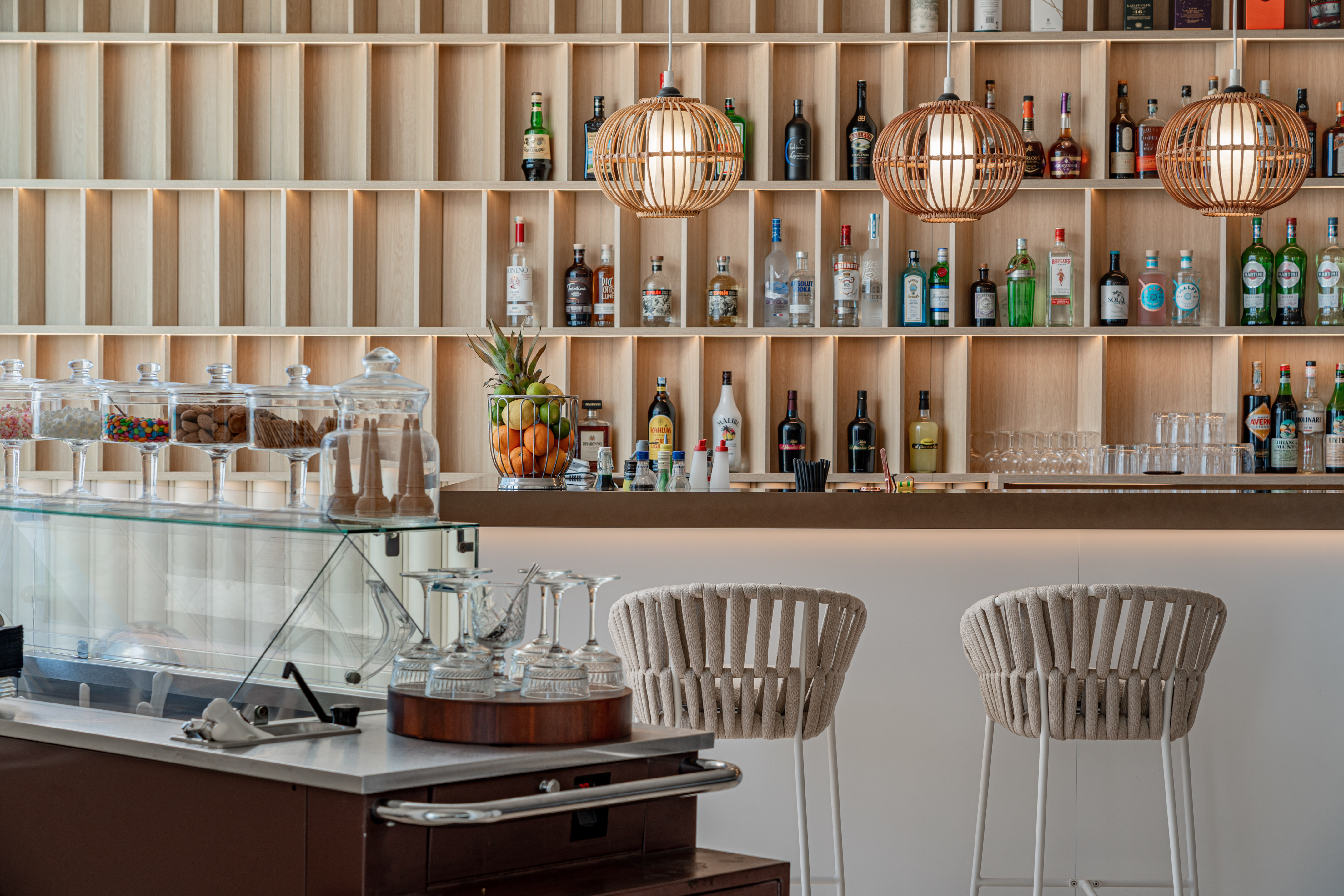 Contemporary bar with wooden liquor shelves, pendant lights, and bar stools.