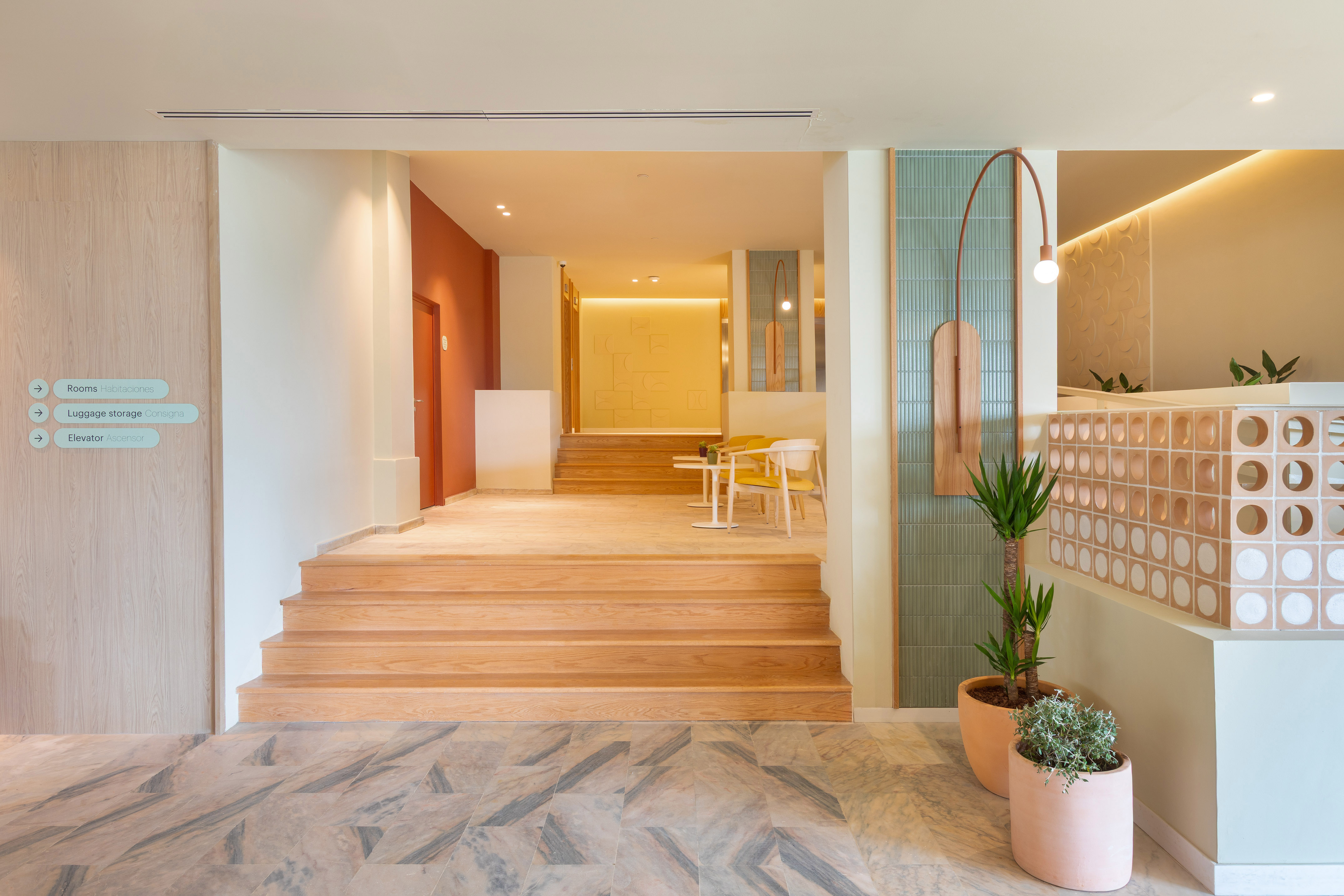 Modern hotel lobby with wooden stairs, marble floor, pastel walls, and signage.