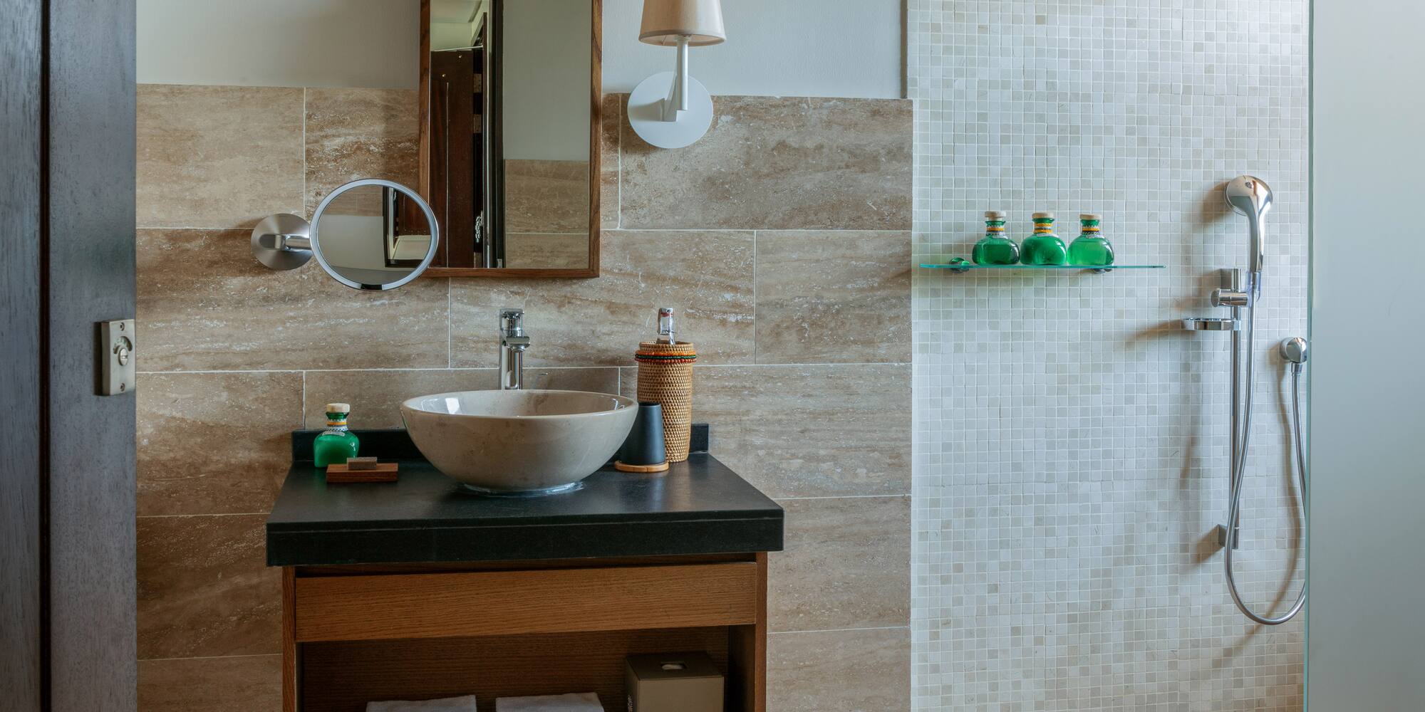 Modern bathroom with stone sink, wood mirror, and walk-in shower with mosaic tiles.