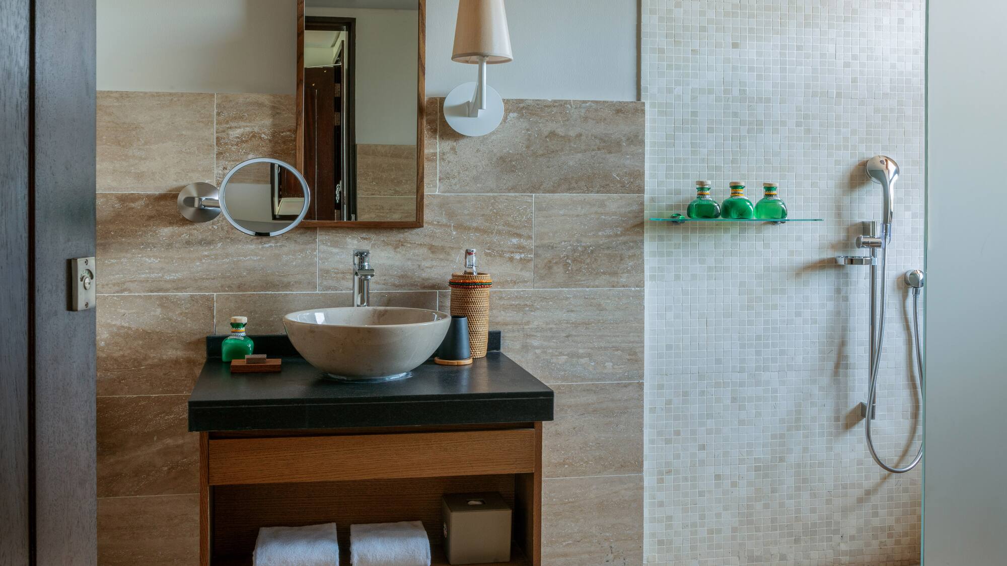 Modern bathroom with stone sink, wood mirror, and walk-in shower with mosaic tiles.