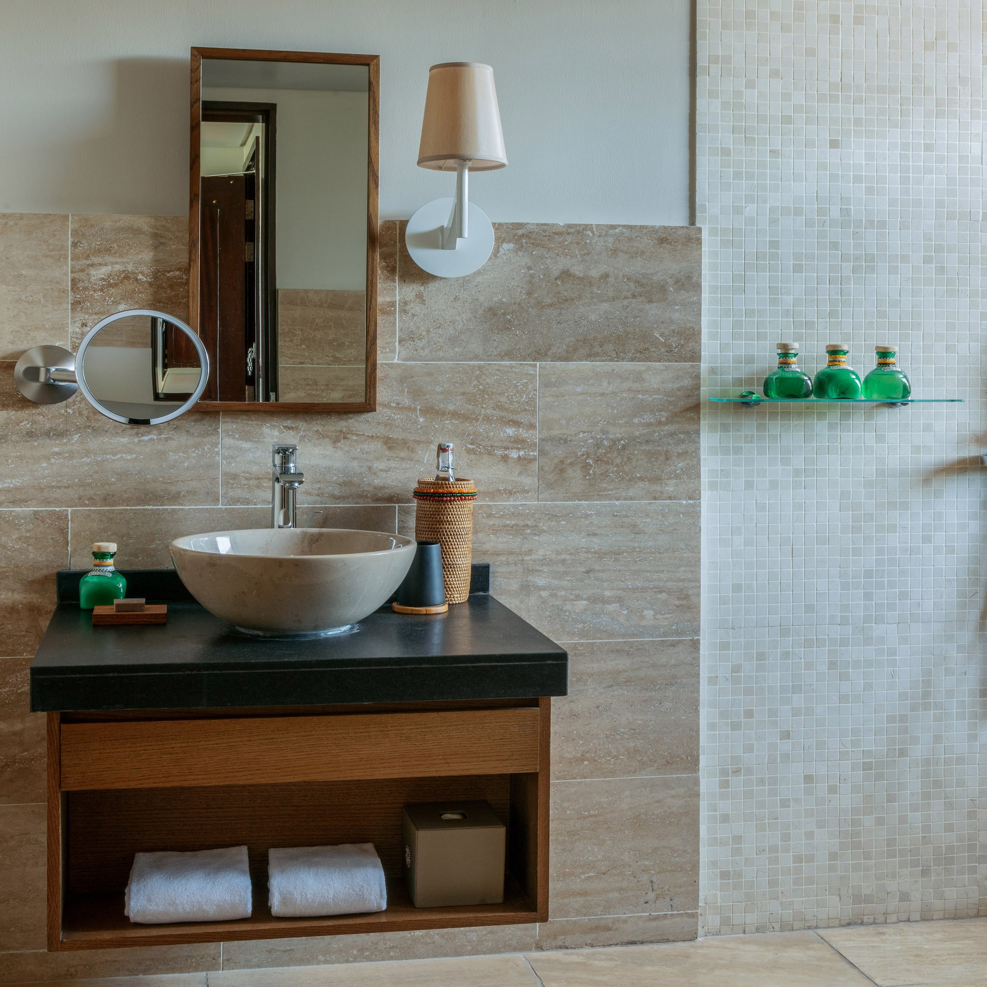 Modern bathroom with stone sink, wood mirror, and walk-in shower with mosaic tiles.