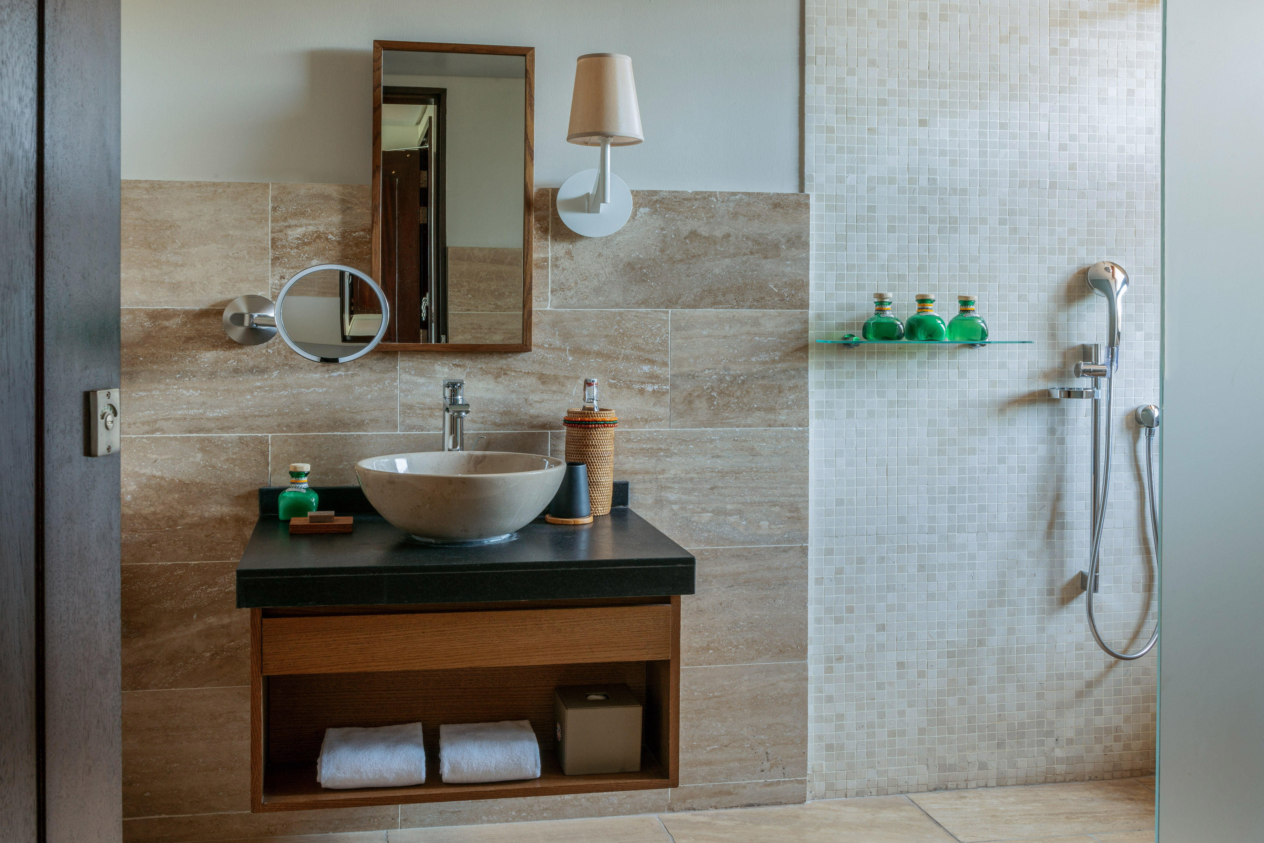 Modern bathroom with stone sink, wood mirror, and walk-in shower with mosaic tiles.