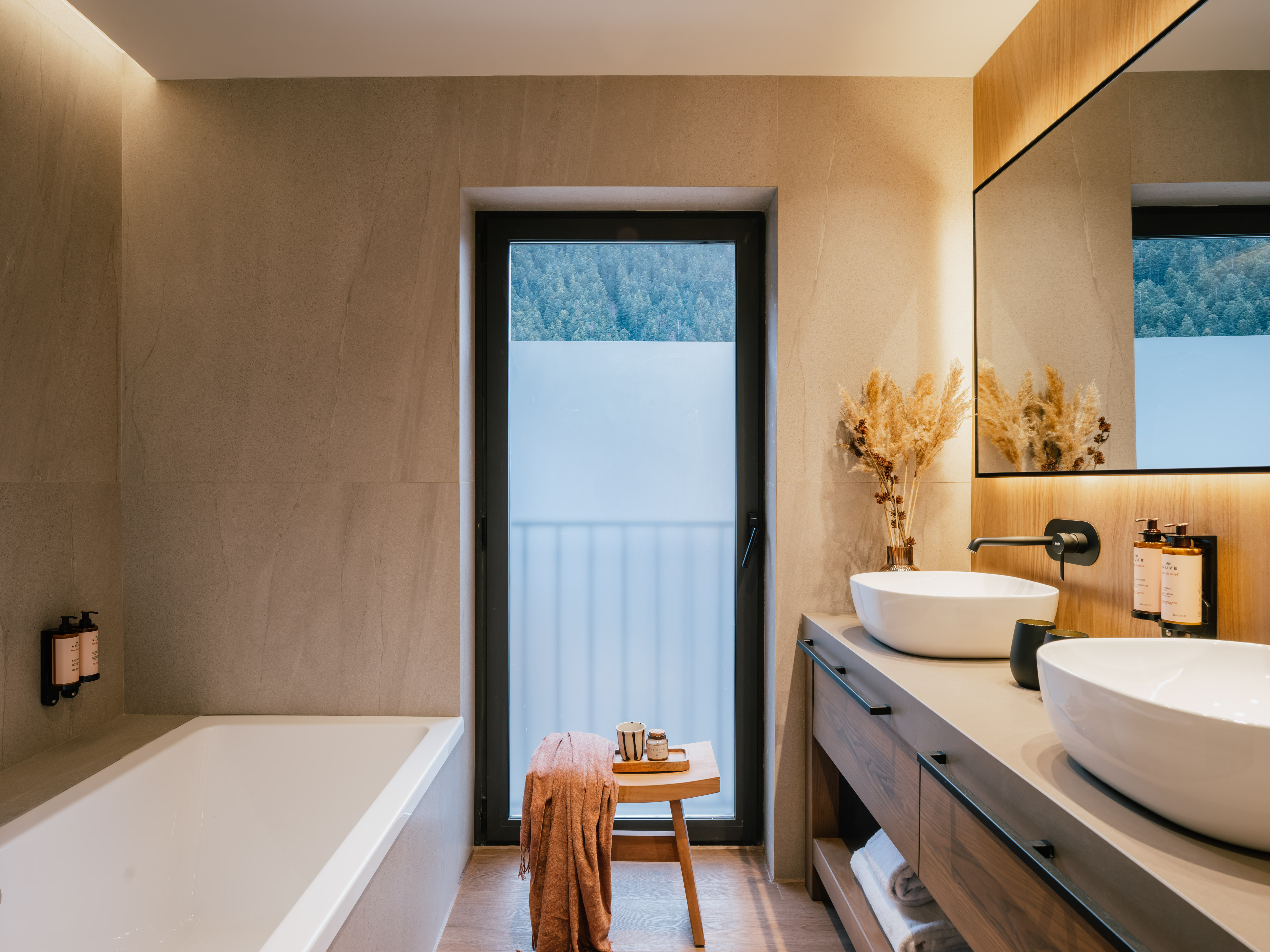 Luxury spa bathroom with forest view, double vanity, and soaking tub.