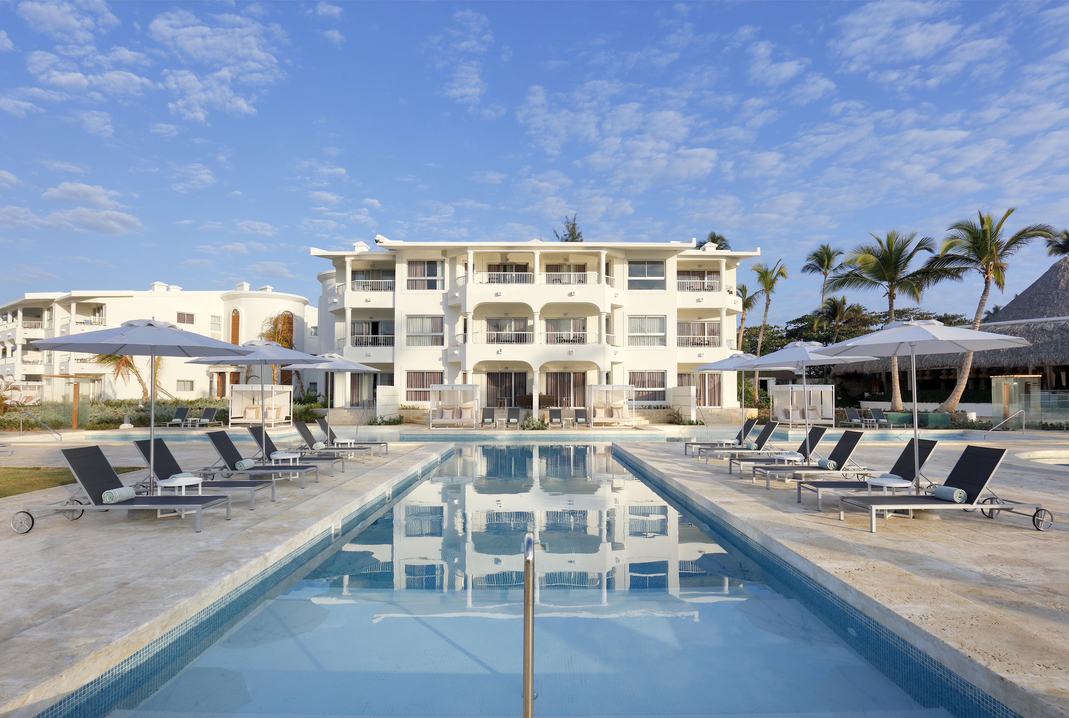 a pool with lounge chairs and umbrellas in front of a building