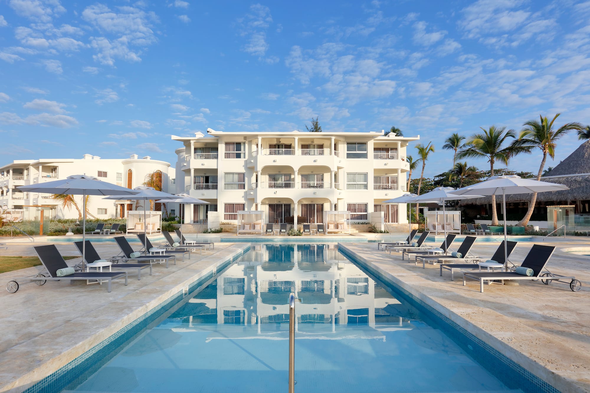 a pool with lounge chairs and umbrellas in front of a building