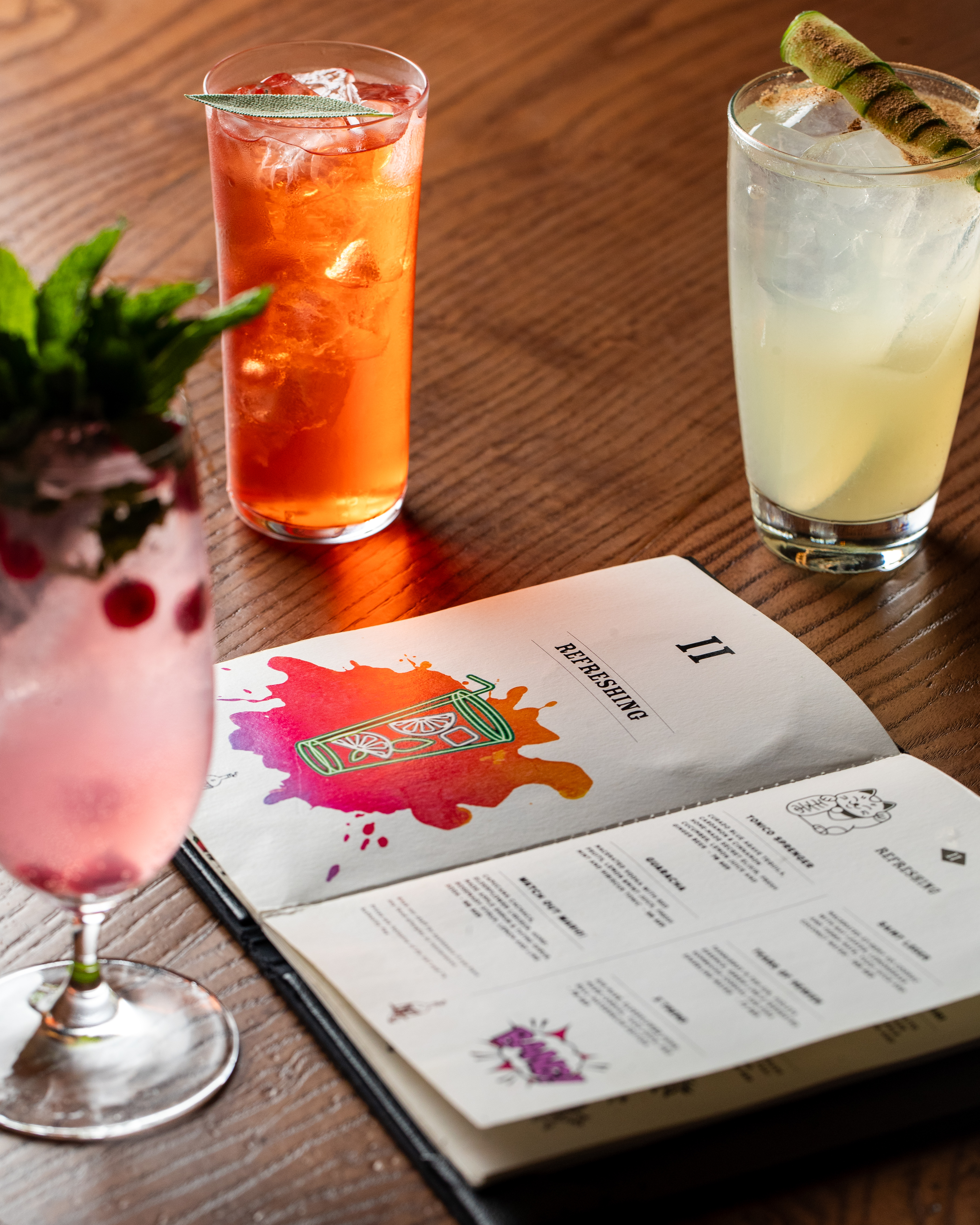 Refreshing cocktails and bar menu with illustrations on a dark wooden table.