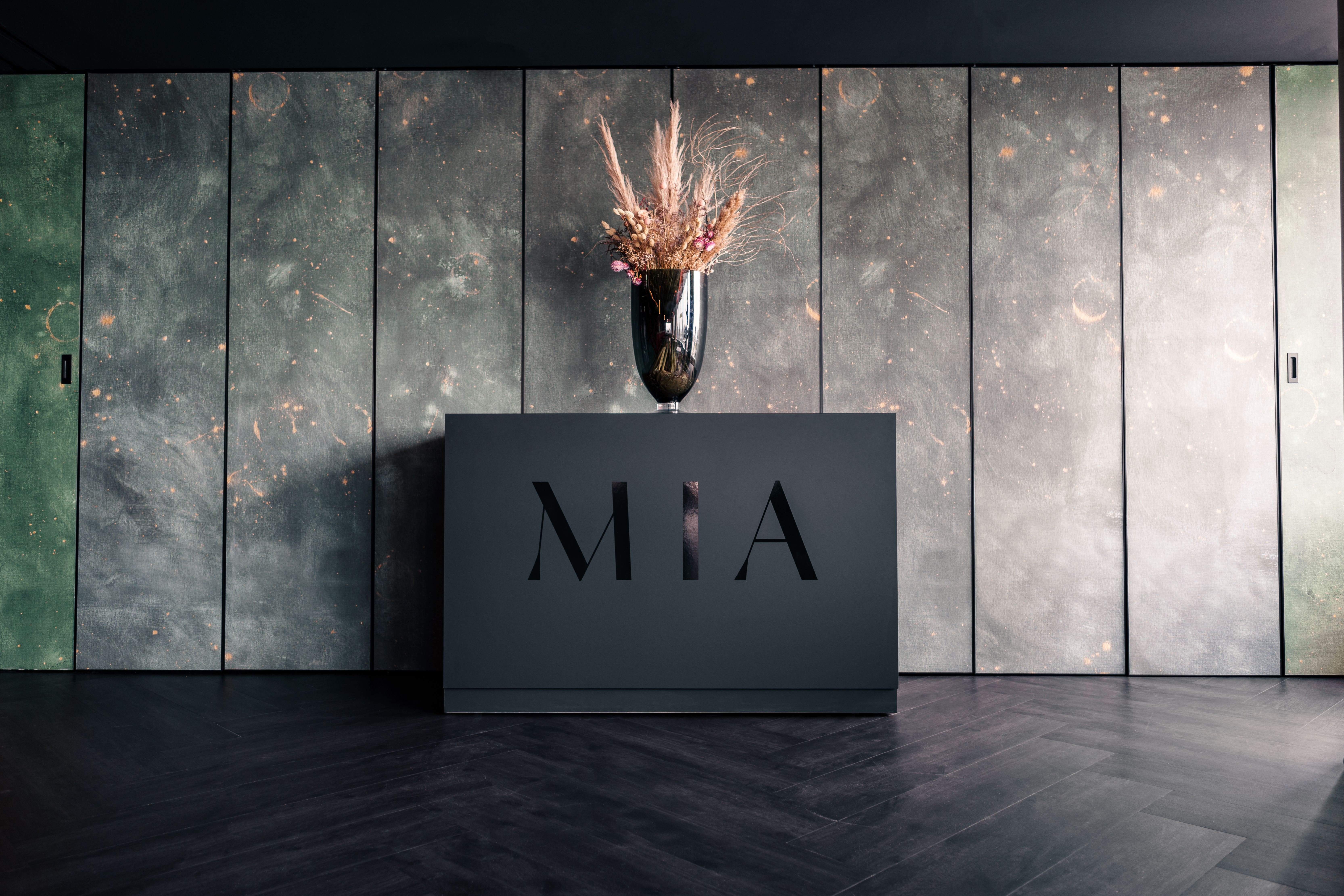 MIA reception desk, dried floral arrangement, dark textured wall, herringbone floor..