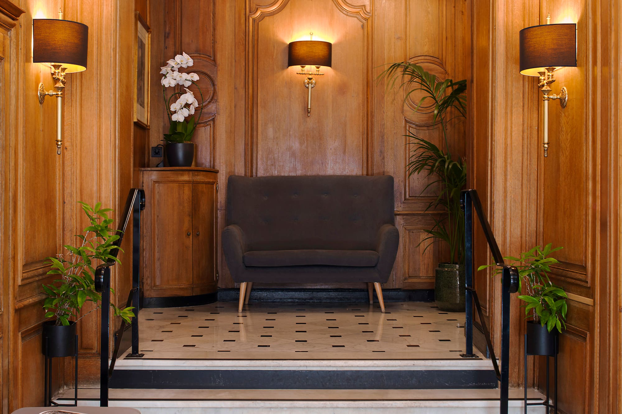 Elegant wood-paneled hotel lobby with marble floor, dark sofa, and staircase.