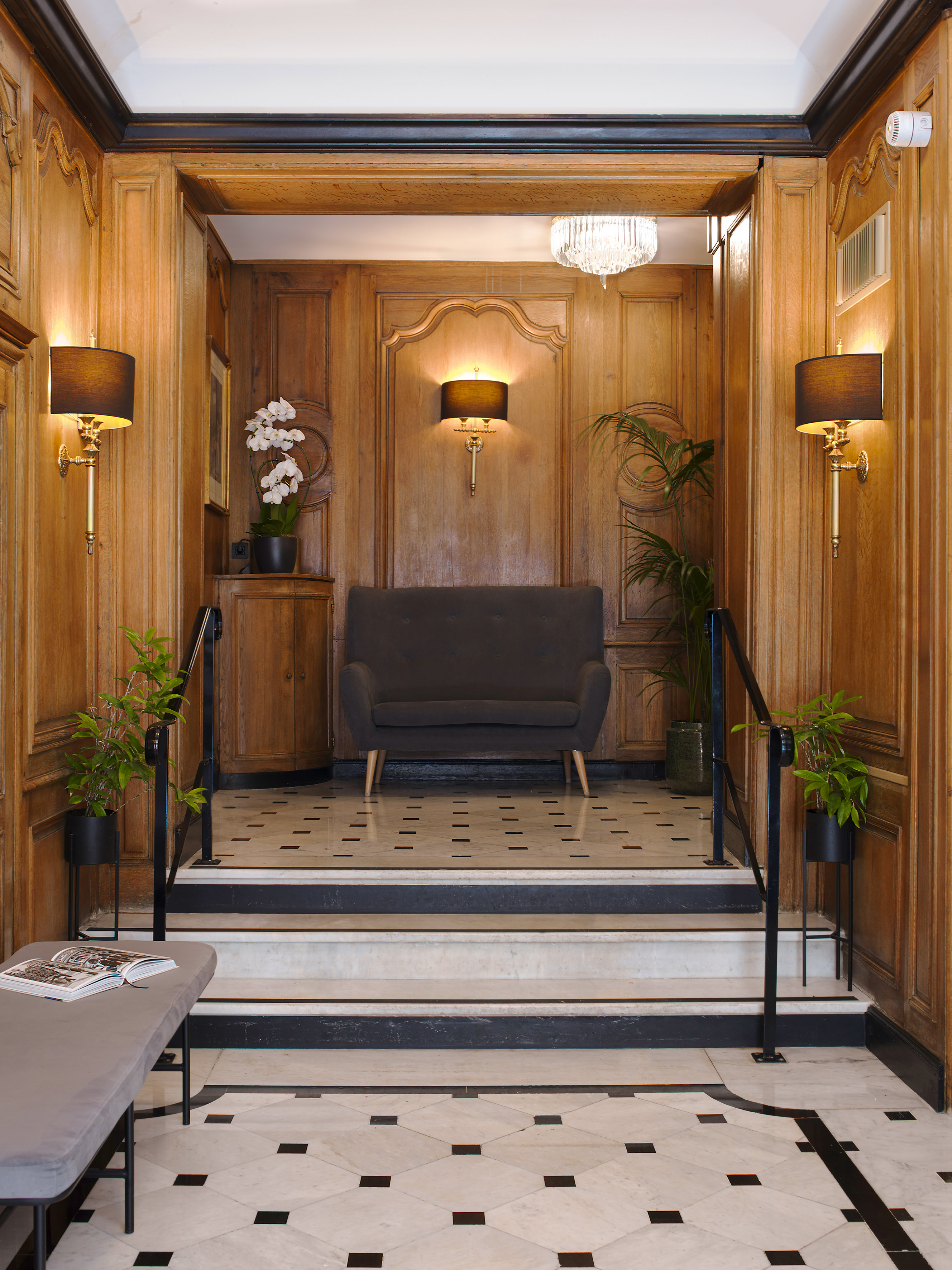 Elegant wood-paneled hotel lobby with marble floor, dark sofa, and staircase.