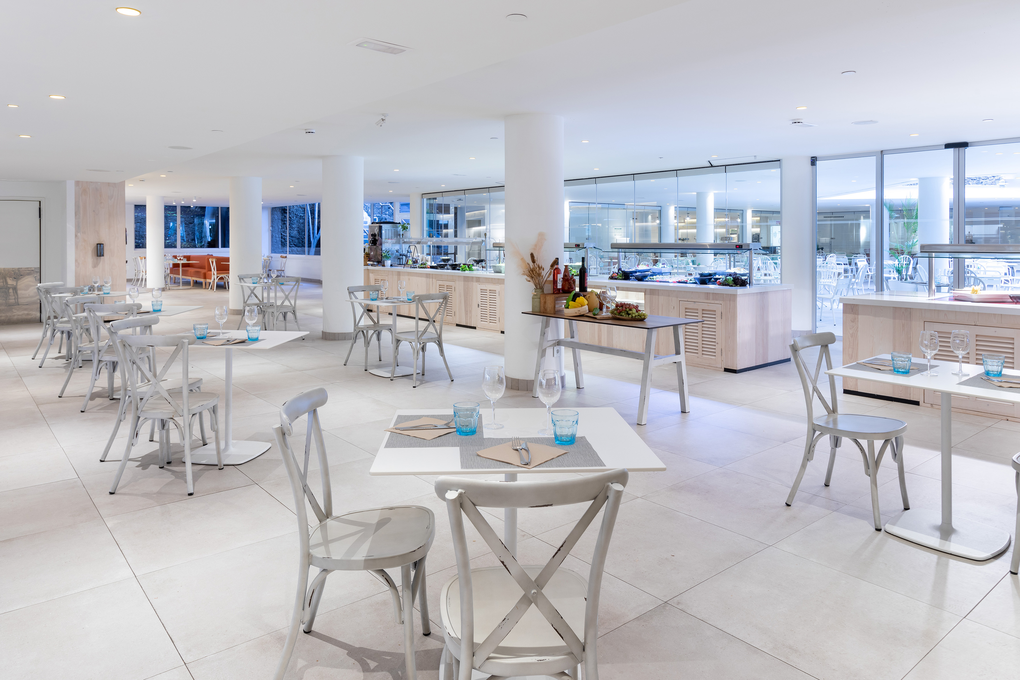 Modern hotel restaurant dining room with white tables, chairs, and buffet counters.