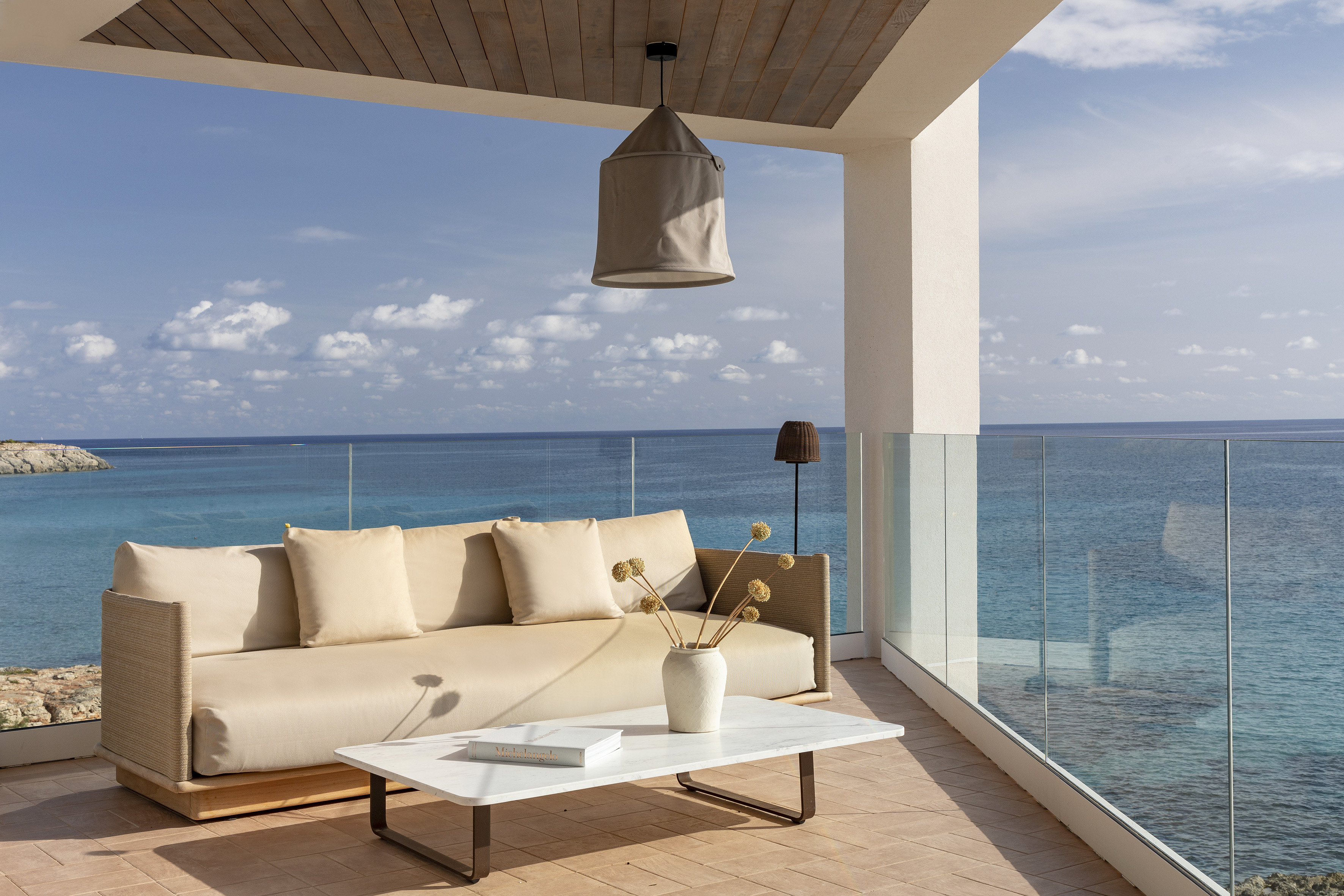 Outdoor sofa on a luxury balcony with stunning ocean view and glass railing.