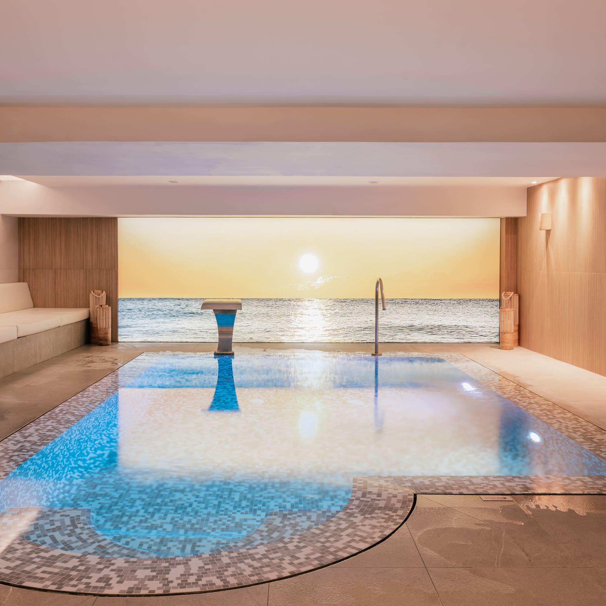 Indoor pool with mosaic tiles, ocean sunset view, luxury spa design.