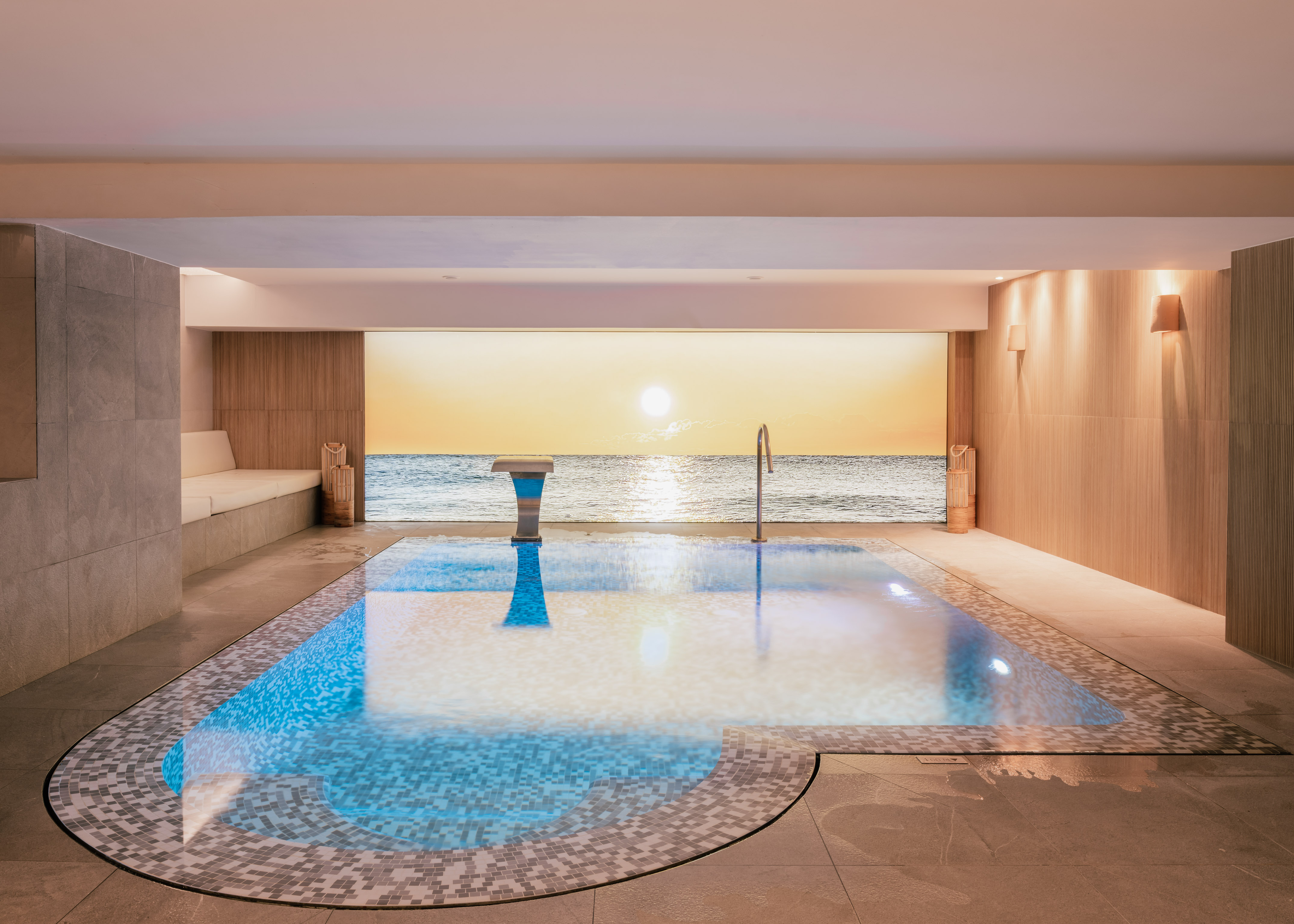 Indoor pool with mosaic tiles, ocean sunset view, luxury spa design.