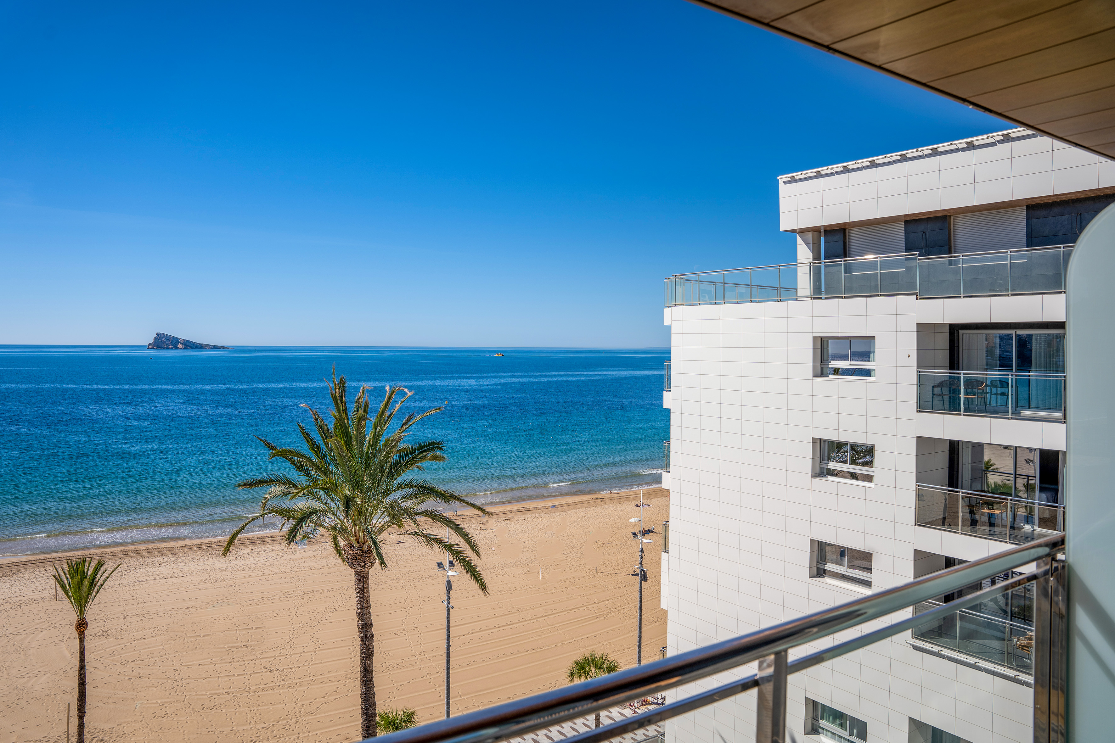 Balcony view of Benidorm beach, blue ocean, palm trees, and modern building.