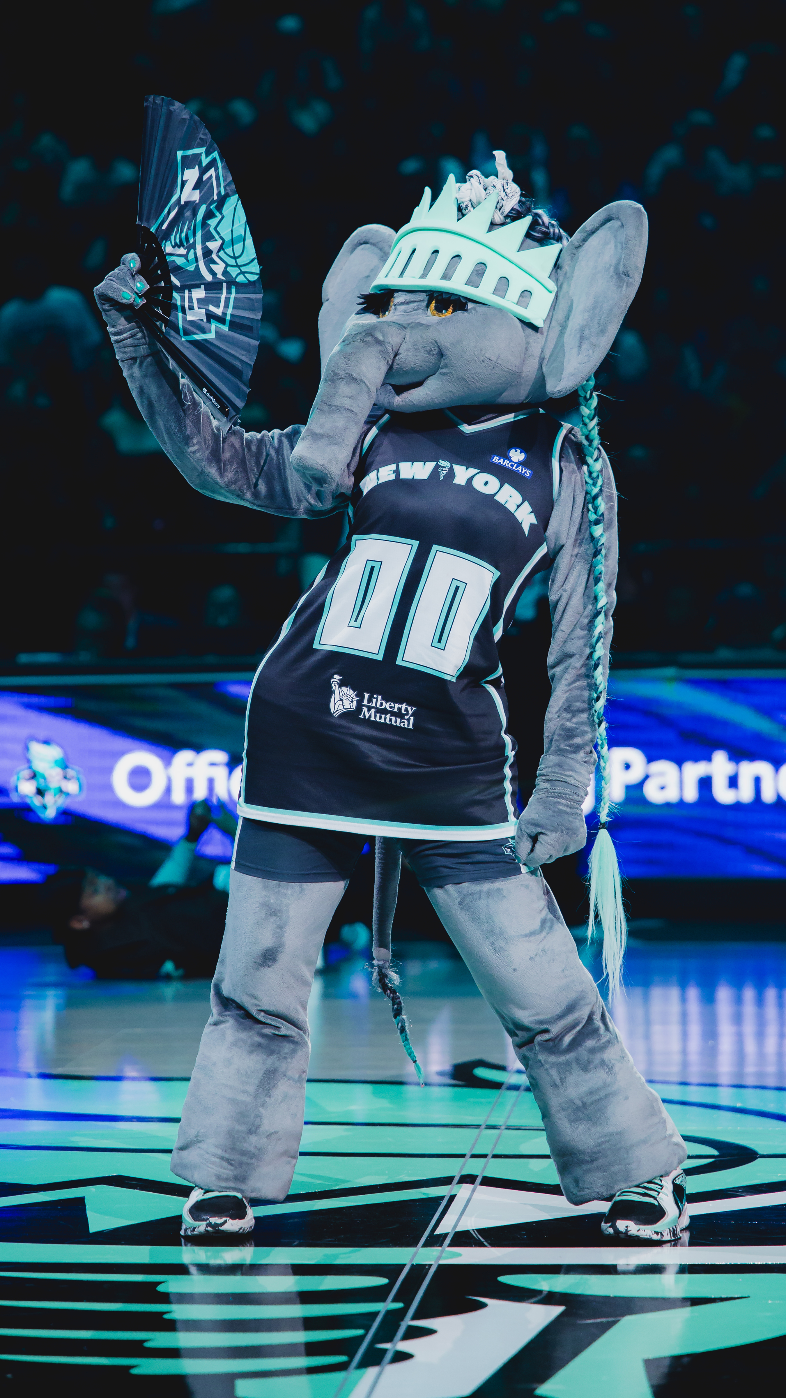 New York Liberty elephant mascot in jersey with Liberty crown, holding fan.