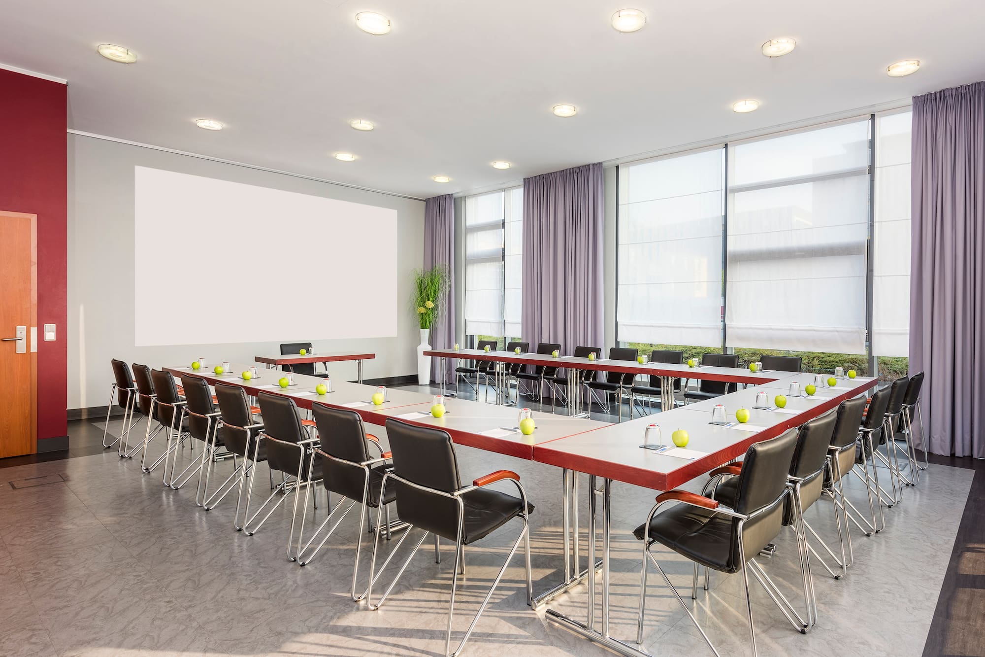 Modern conference room with U-shaped table, blank screen, and large windows.