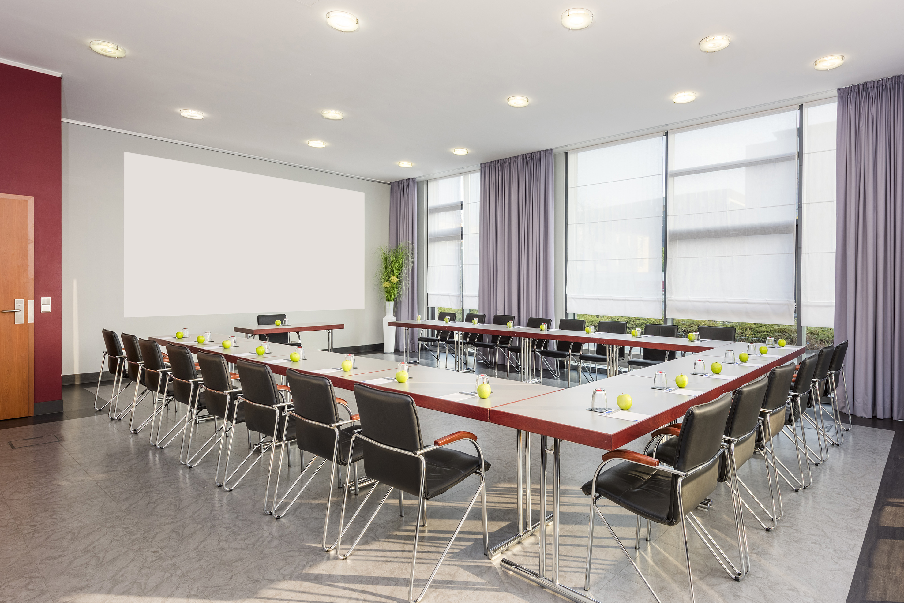 Modern conference room with U-shaped table, blank screen, and large windows.