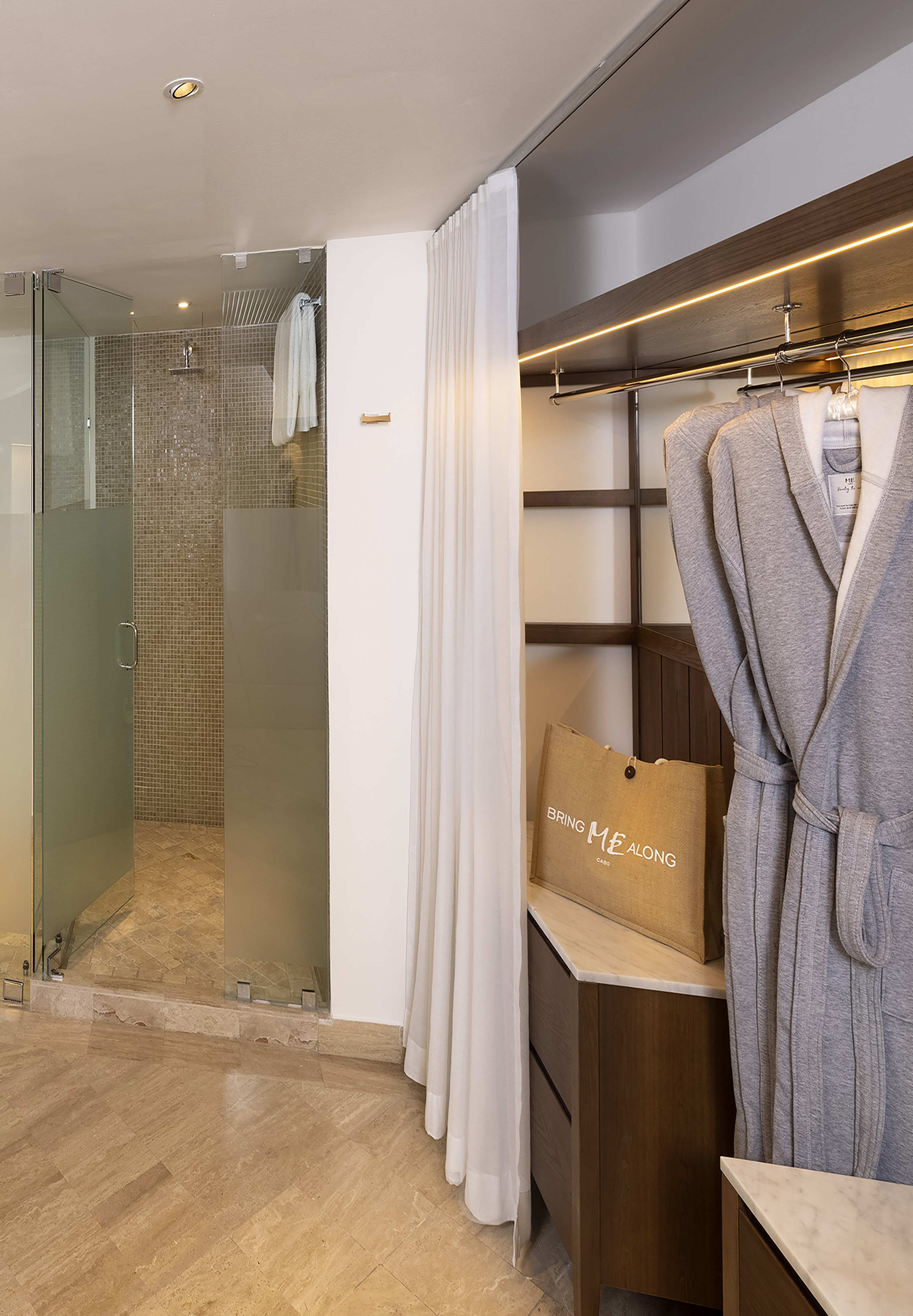 Modern hotel bath and closet with glass shower, mosaic tiles, and bathrobes.