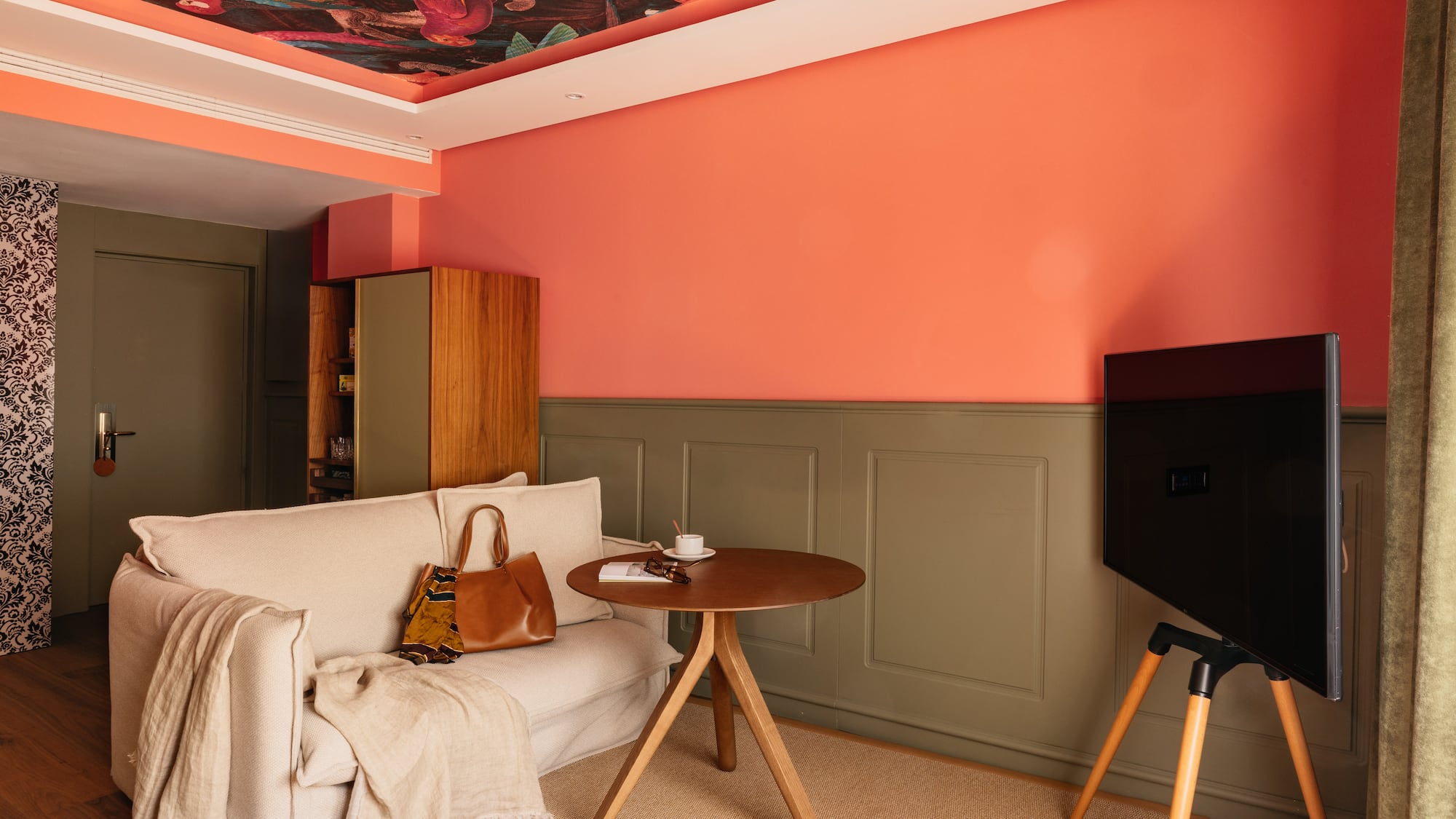Sala de estar moderna: paredes salmón, sofá beige, TV y techo botánico.