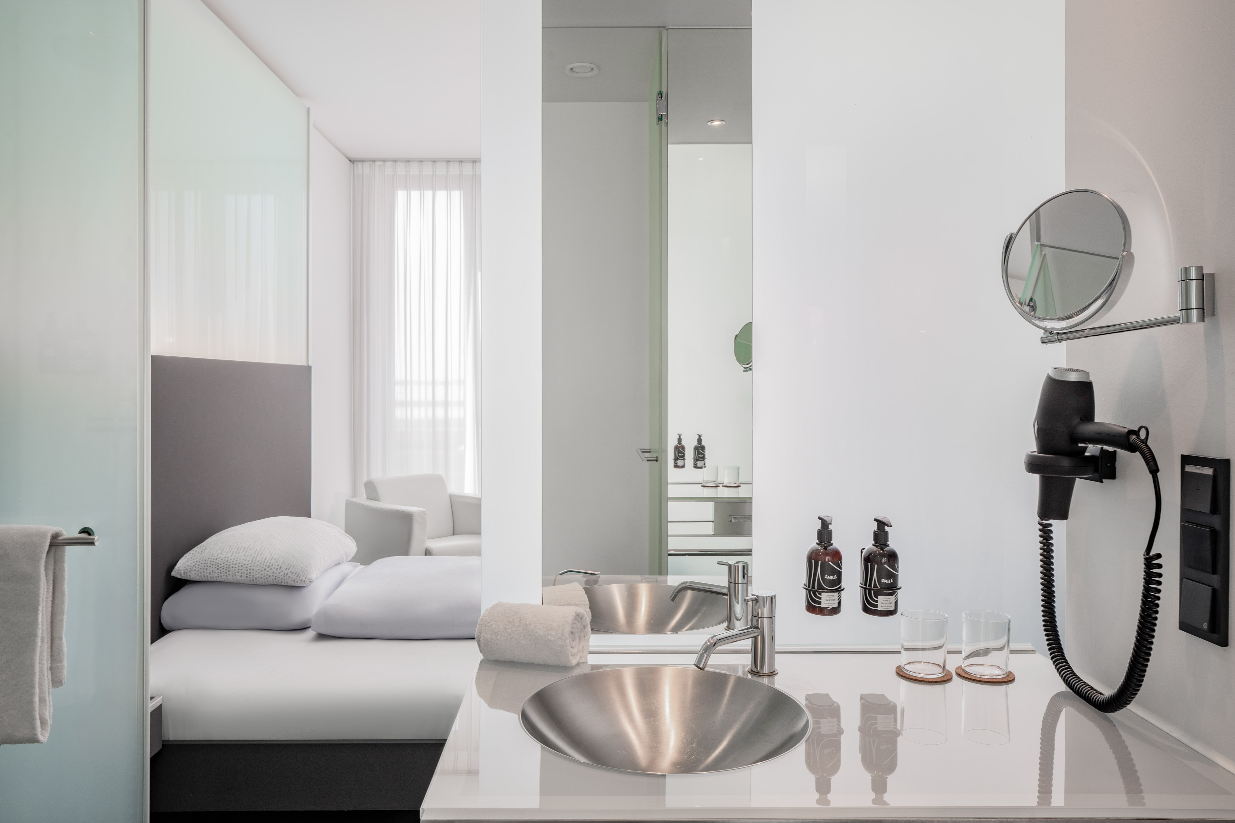 Minimalist hotel suite featuring open bathroom vanity, bed, and bright interior.