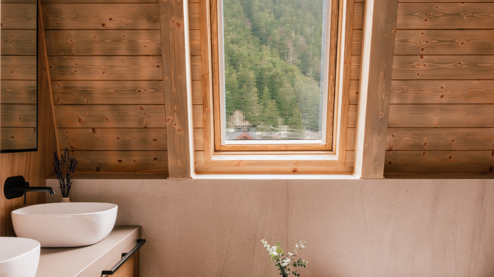 Rustic wood paneled bathroom with forest view, double vanity, and bathtub.