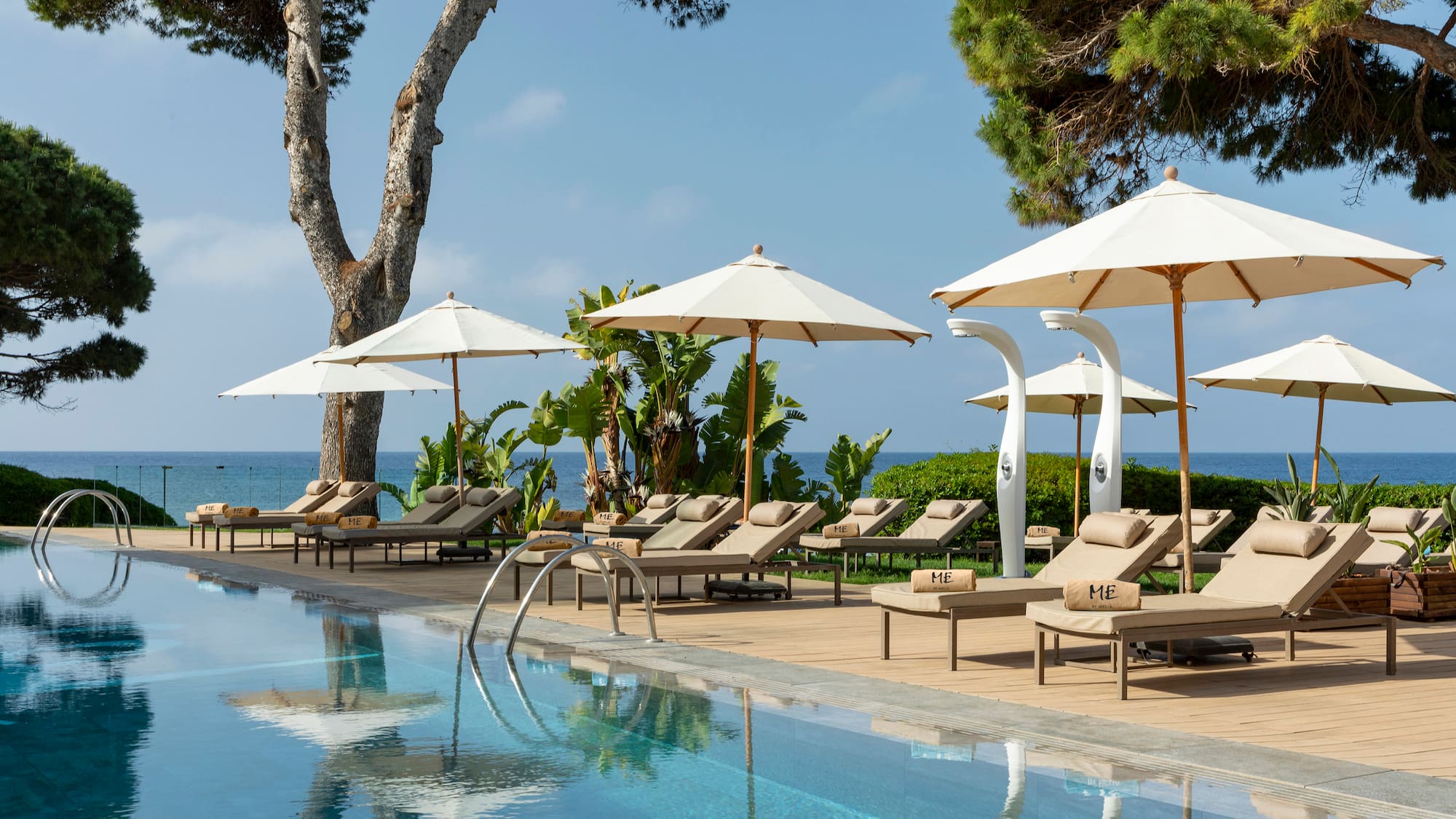 Outdoor resort pool with sun loungers, white umbrellas, and ocean vista.