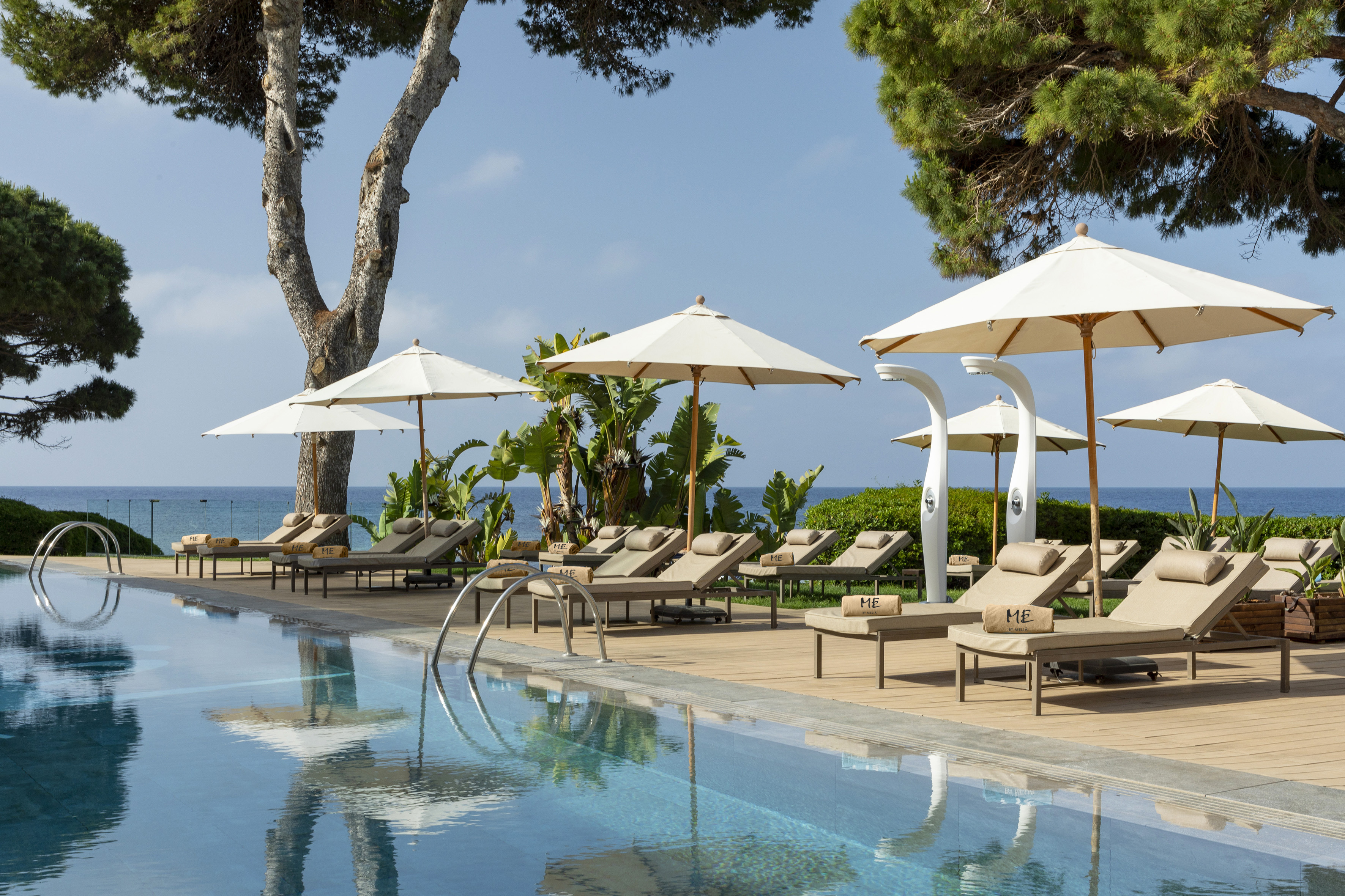 Luxury hotel pool with sun loungers, umbrellas, and ocean view.
