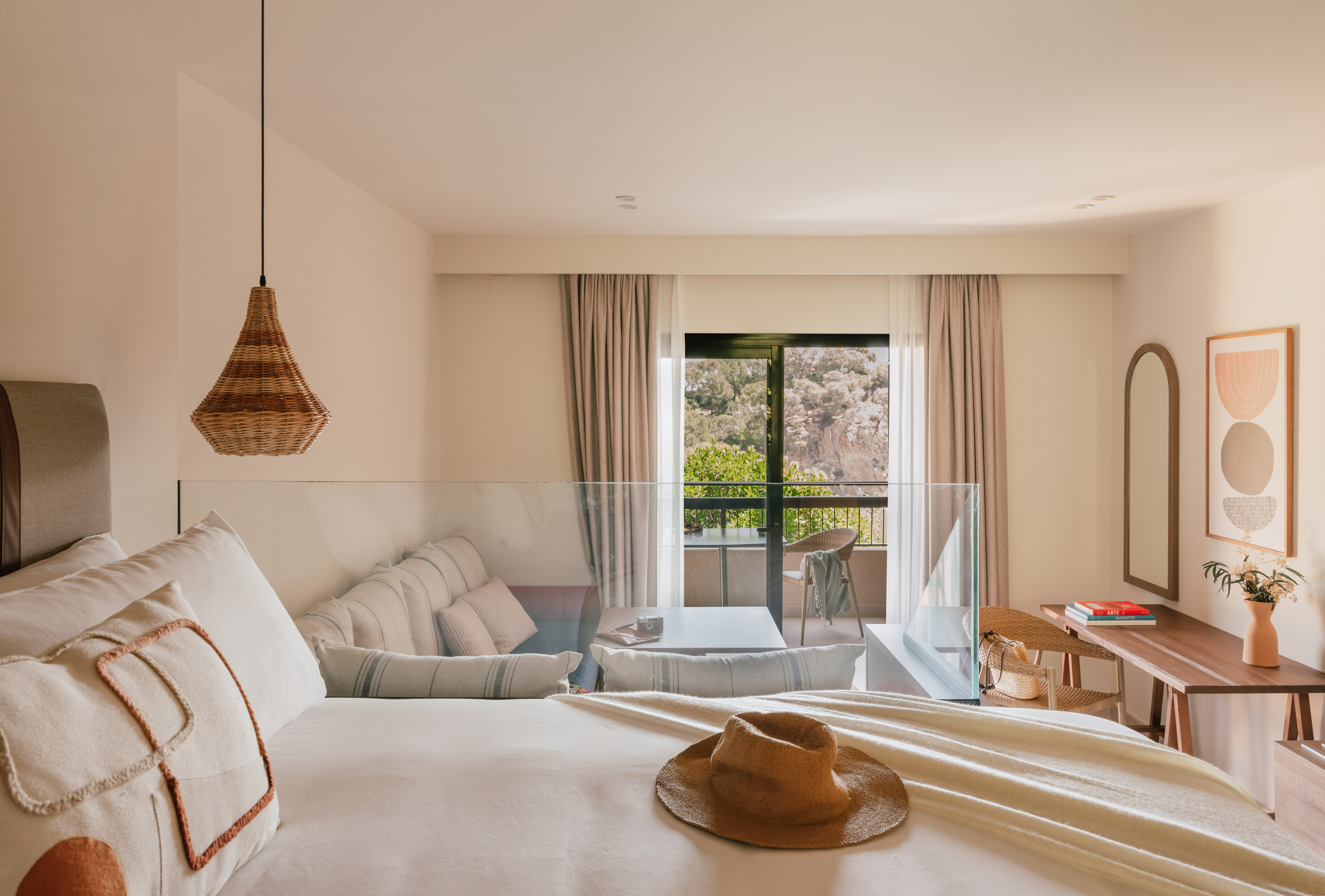 Luxury hotel room with balcony, king bed, straw hat, and scenic mountain view.