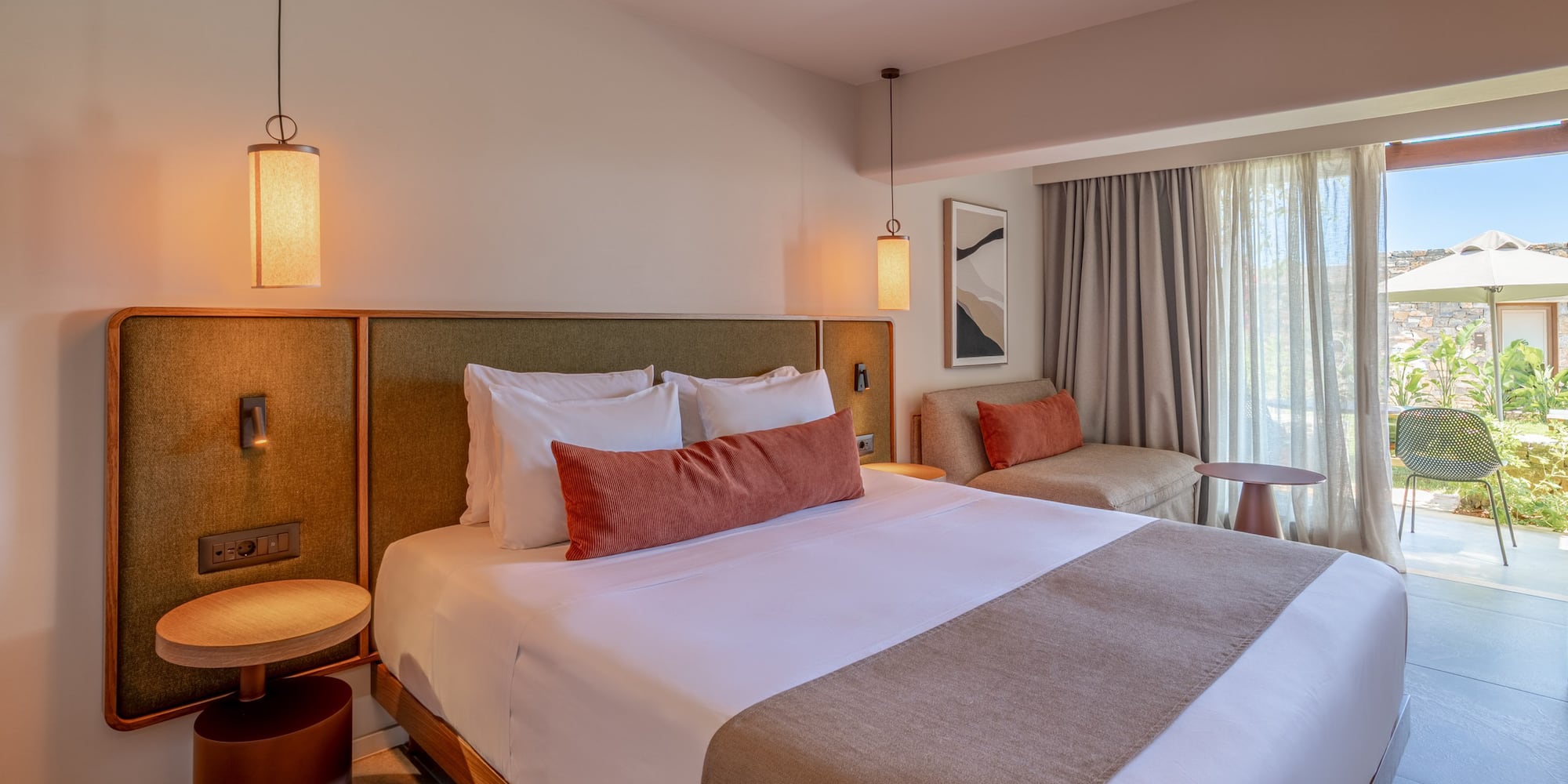 Modern hotel bedroom with king bed, sofa, and patio garden view.