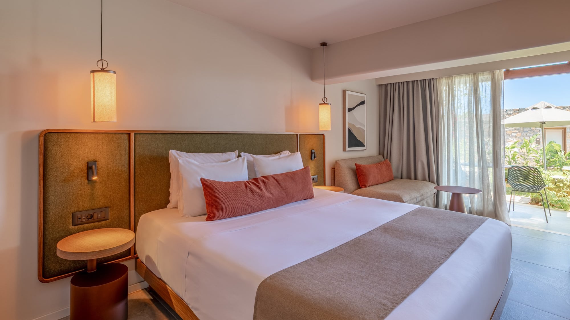 Modern hotel bedroom with king bed, sofa, and patio garden view.