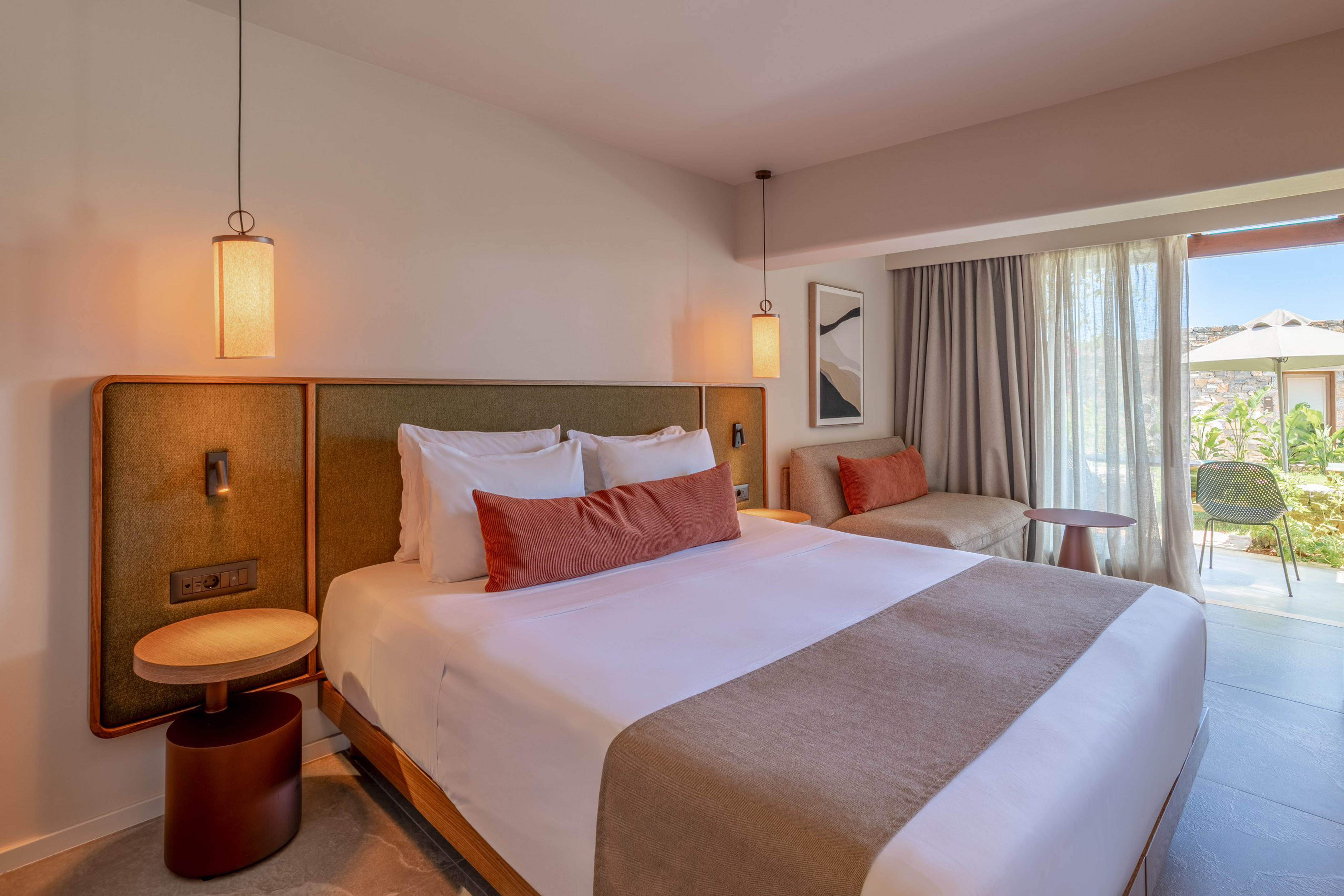 Modern hotel bedroom with king bed, sofa, and patio garden view.