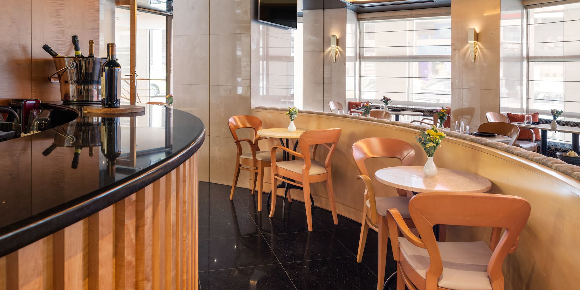 Elegant hotel restaurant bar with modern tables, wooden chairs, and wine display.