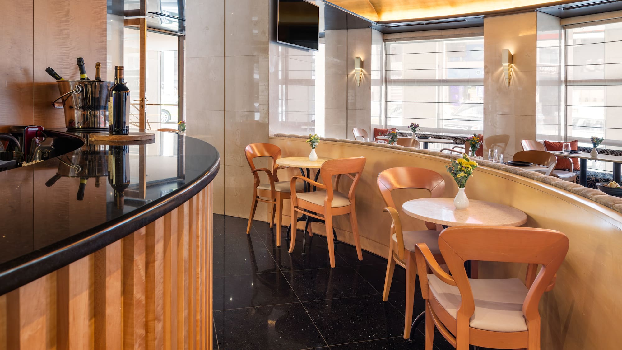 Elegant hotel restaurant bar with modern tables, wooden chairs, and wine display.