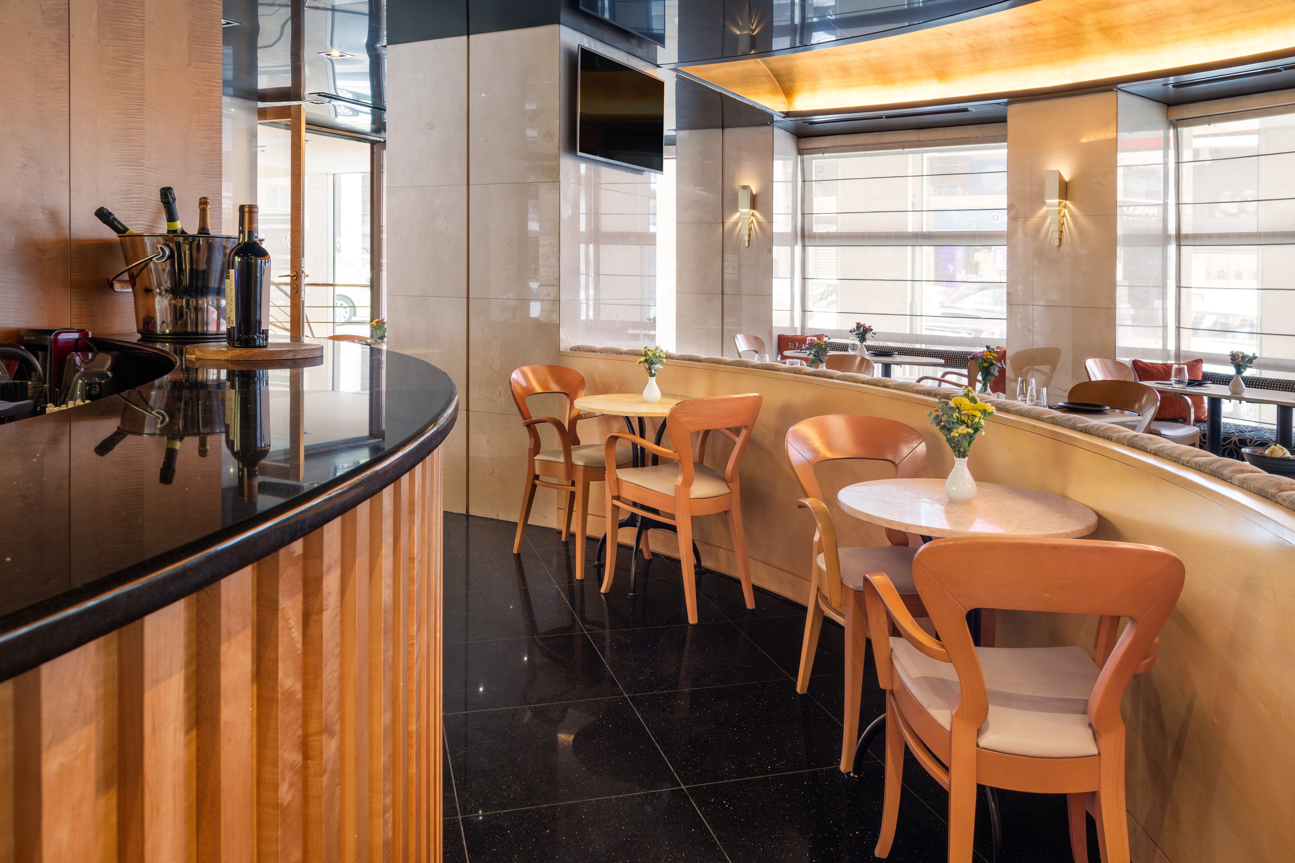 Elegant hotel restaurant bar with modern tables, wooden chairs, and wine display.