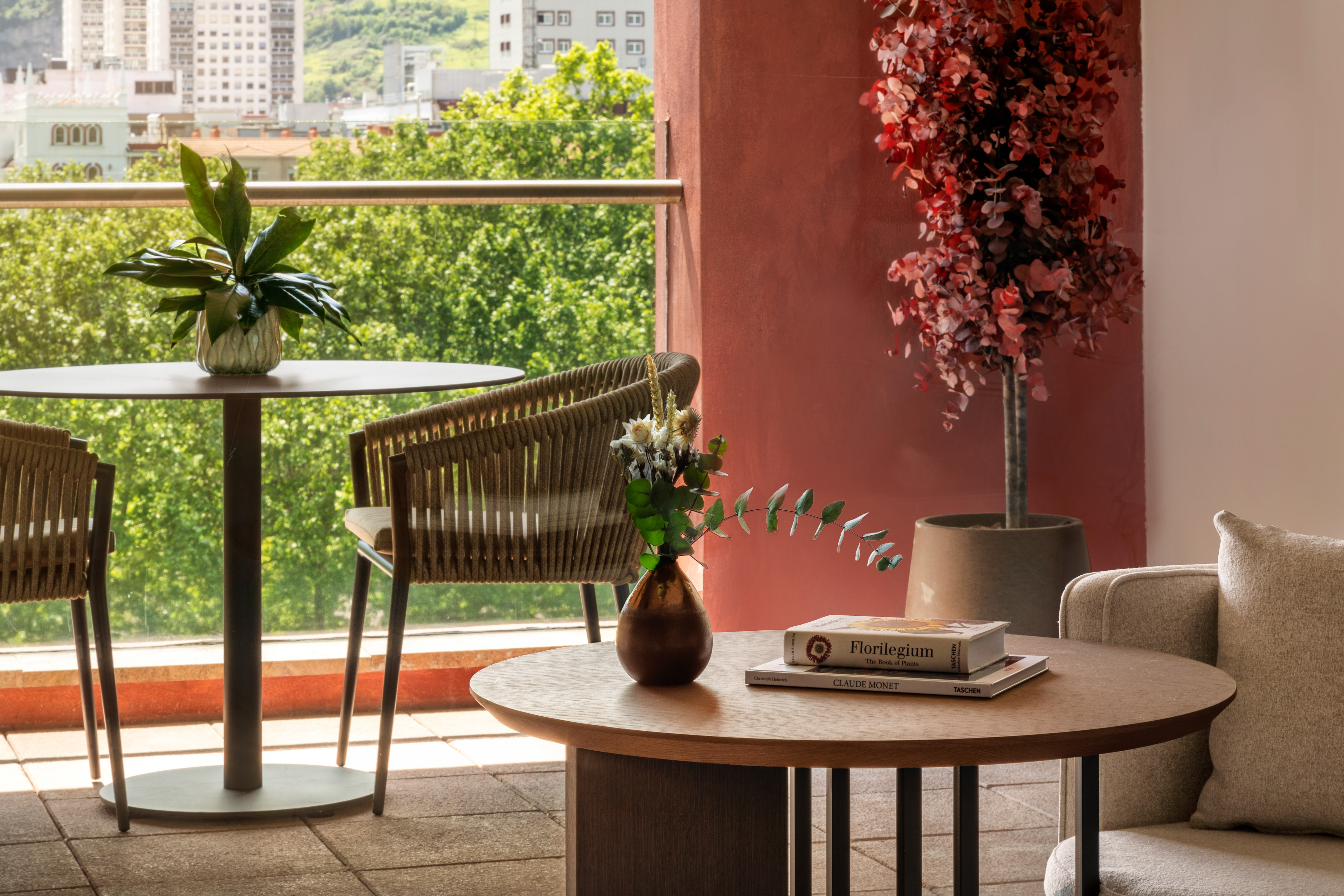 Modern balcony with outdoor seating, red wall, potted plants, and city view.