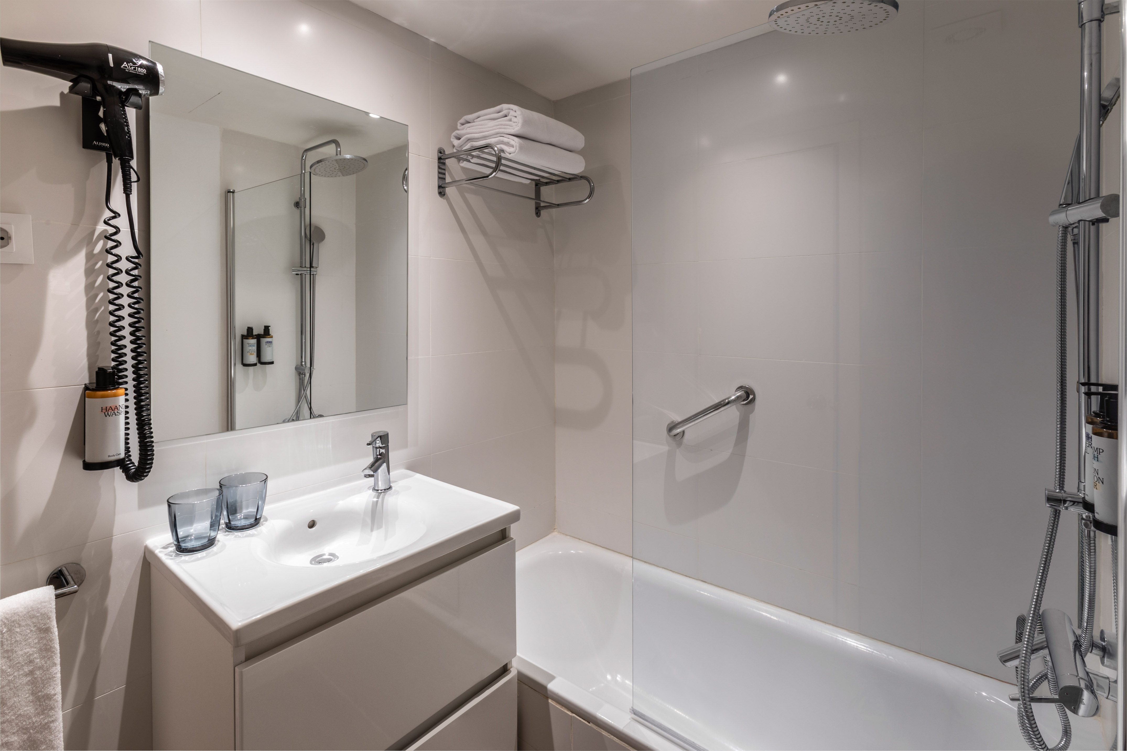 White modern bathroom with sink, mirror, hairdryer, bathtub, and rain shower.