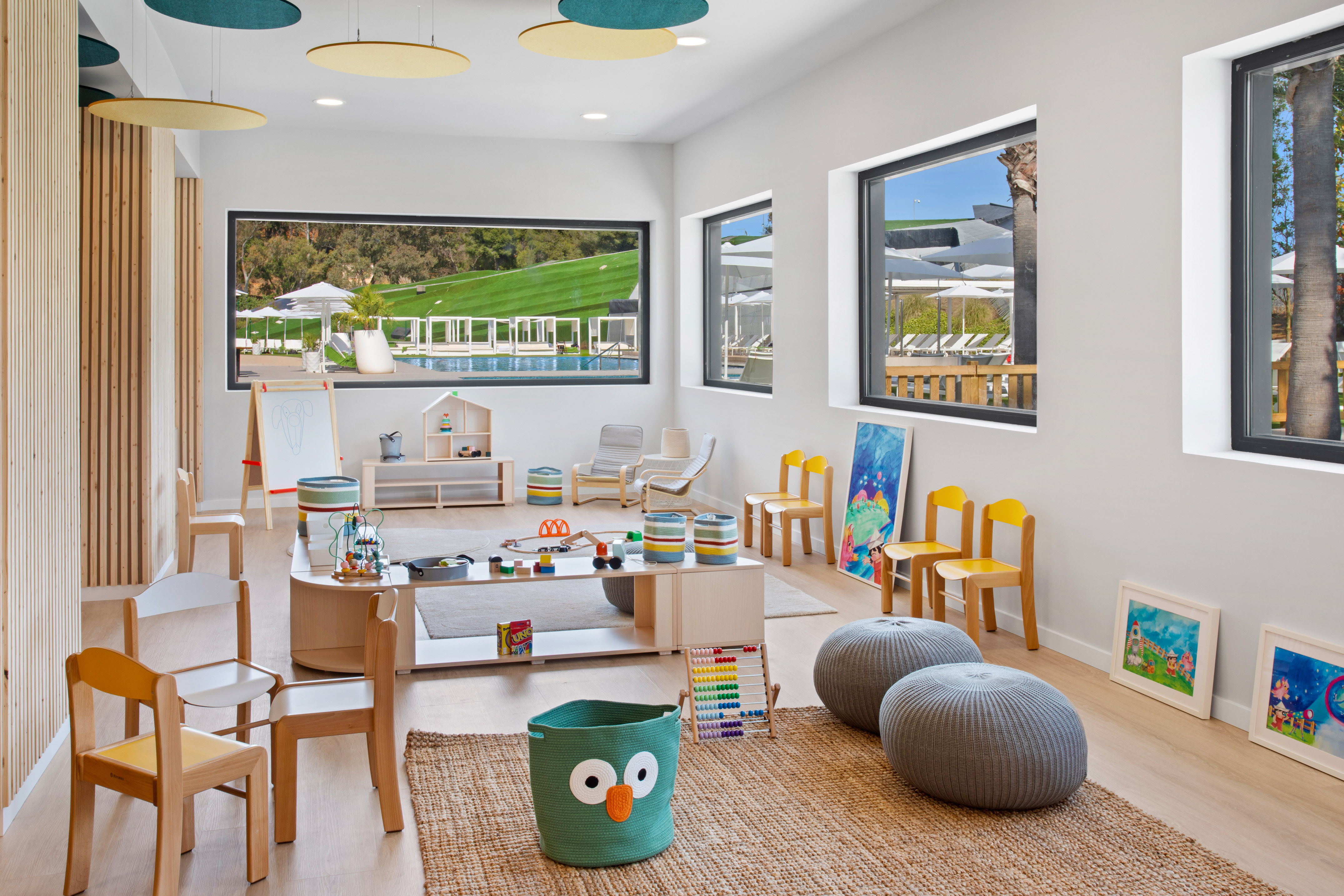 Modern kids' club playroom with colorful toys, small chairs, pool view.