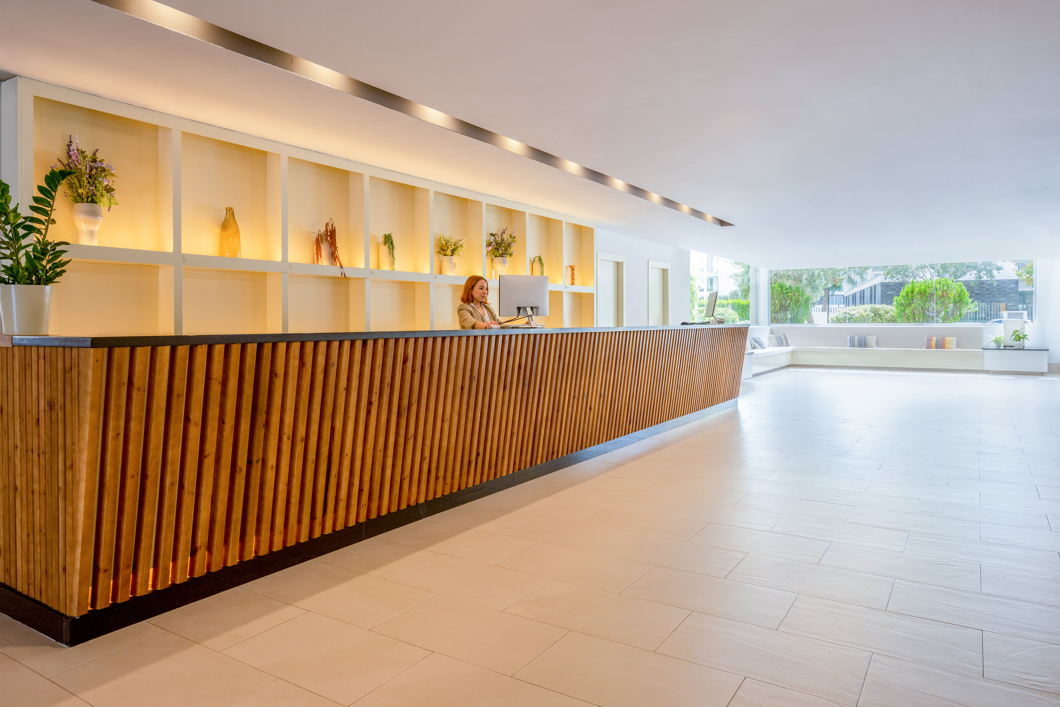 Modern hotel reception desk with a female receptionist in a bright lobby.